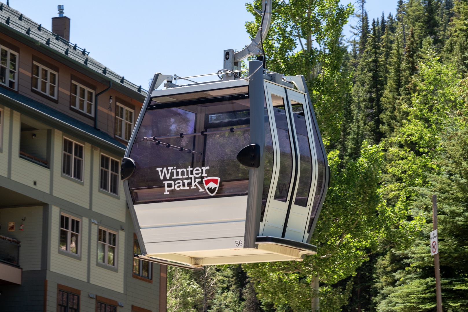A scenic gondola marked Winter Park glides above the property, surrounded by lush evergreen forest and alpine charm during a bright summer day.
