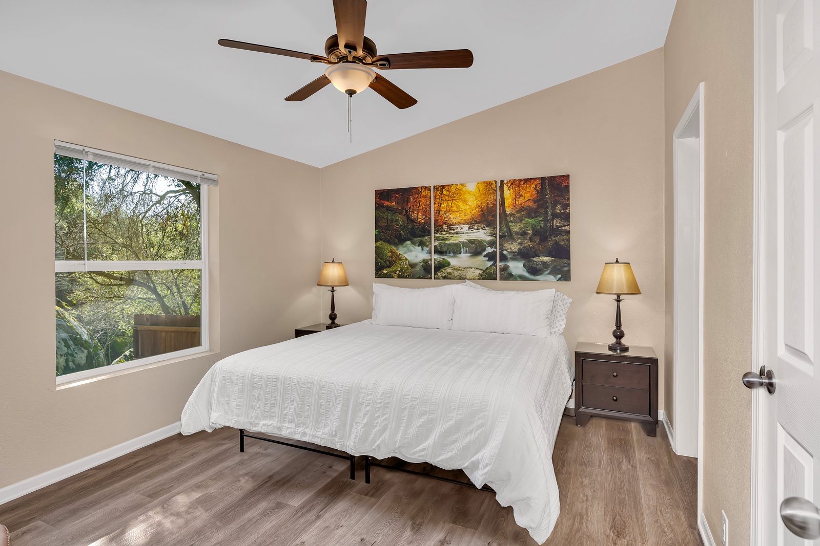 Drift off on a new luxury King mattress in your serene primary bedroom with crisp linens, gentle ceiling fan, and peaceful tree views.