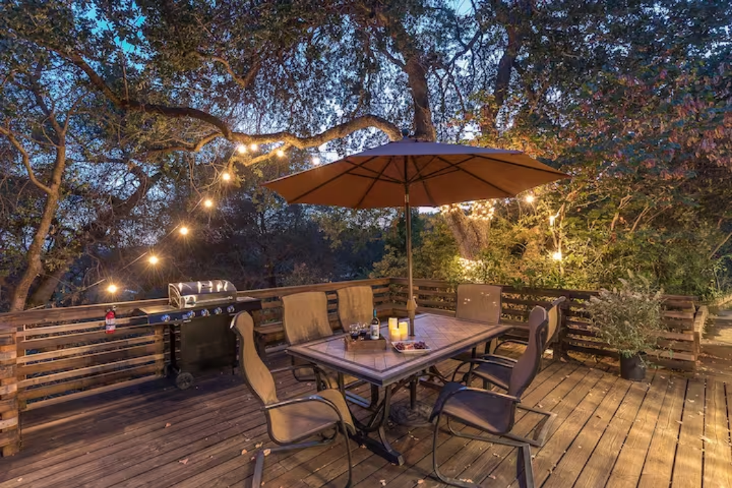 Your private deck glows with string lights, perfect for evening BBQs under the umbrella surrounded by trees.