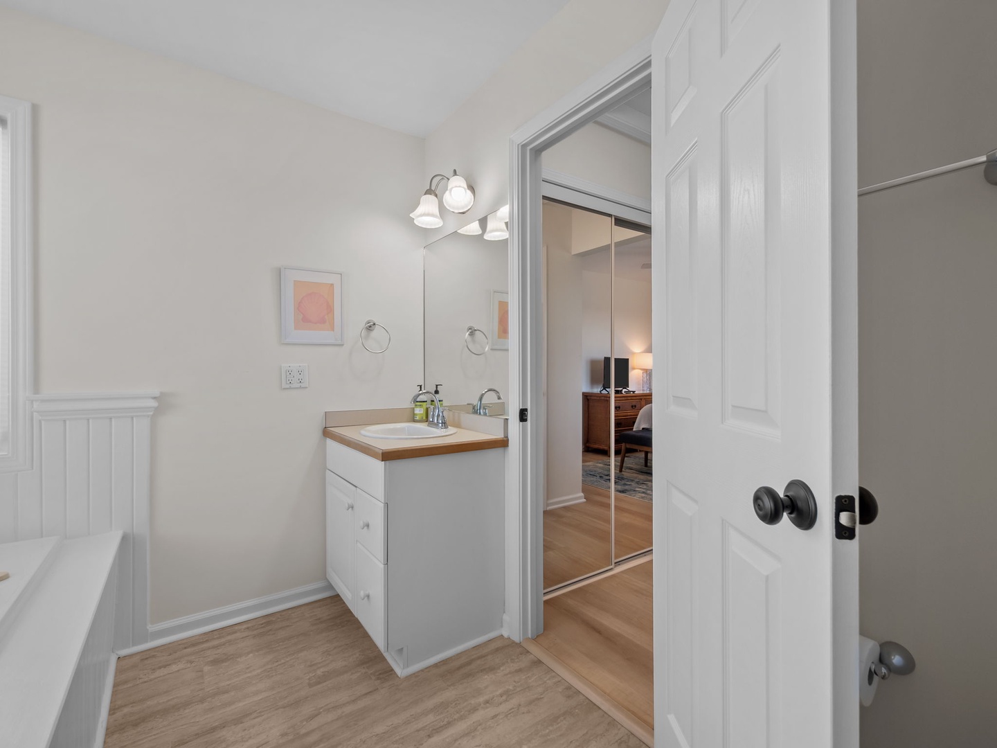 Your bright bathroom features clean white cabinetry, warm wood-look floors, and thoughtful details like framed art to make your daily routine feel special.