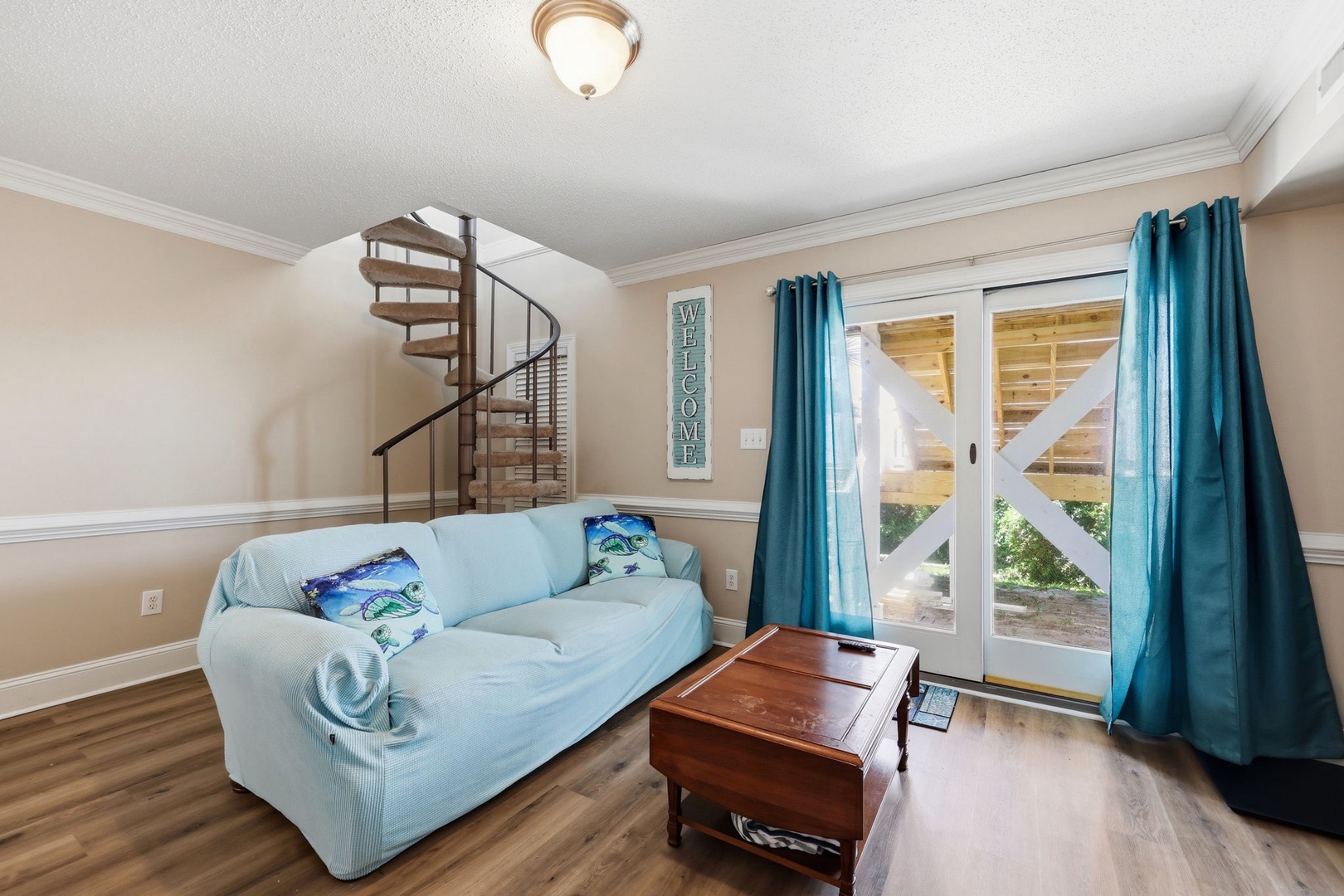 Unwind on your cozy sofa while natural light pours through glass doors, revealing a charming porch view. A spiral staircase adds character, inviting you to explore upstairs.