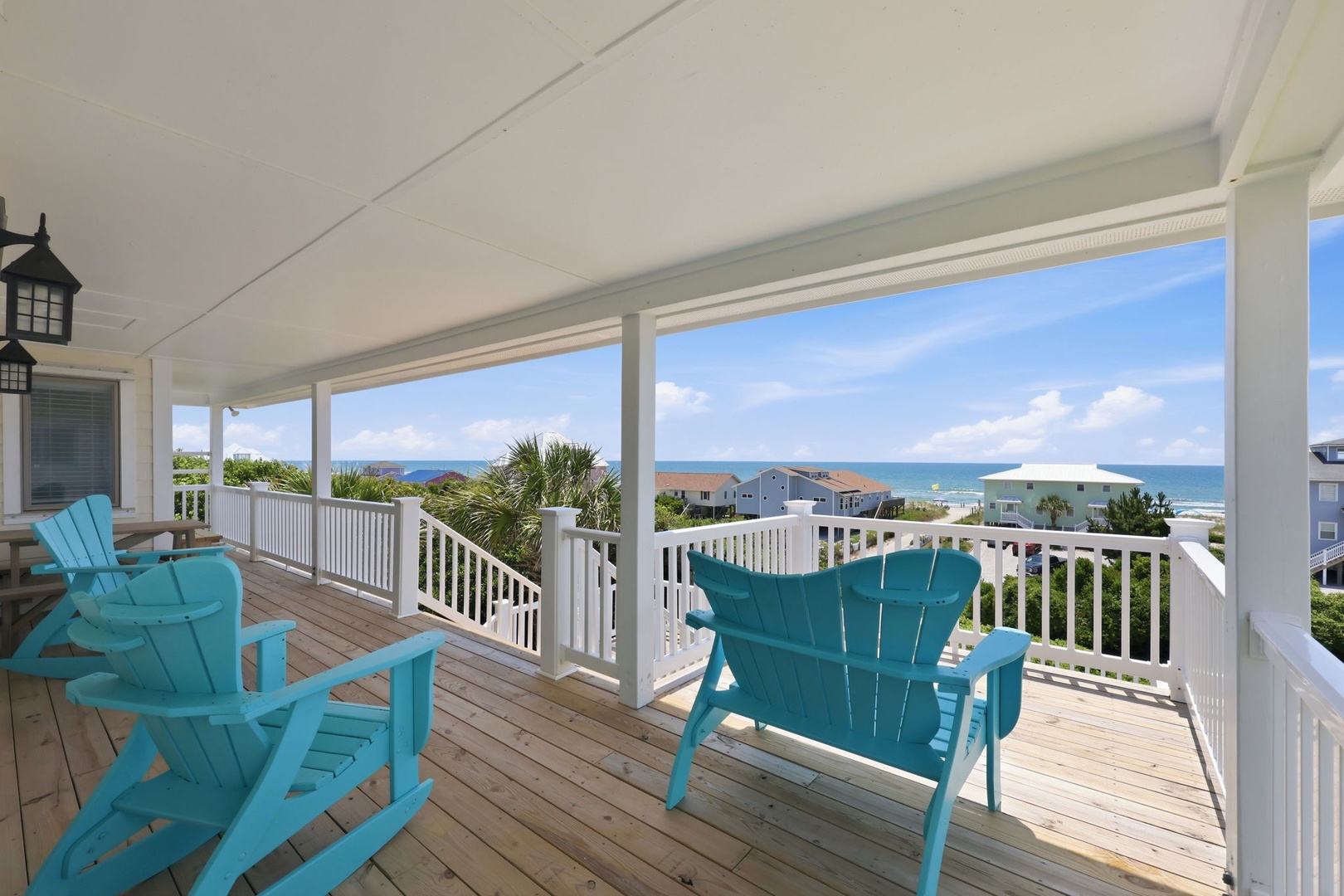 Your covered porch offers a stunning seaside retreat with turquoise Adirondack chairs framing breathtaking ocean views, perfect for morning coffee or sunset cocktails in coastal comfort.
