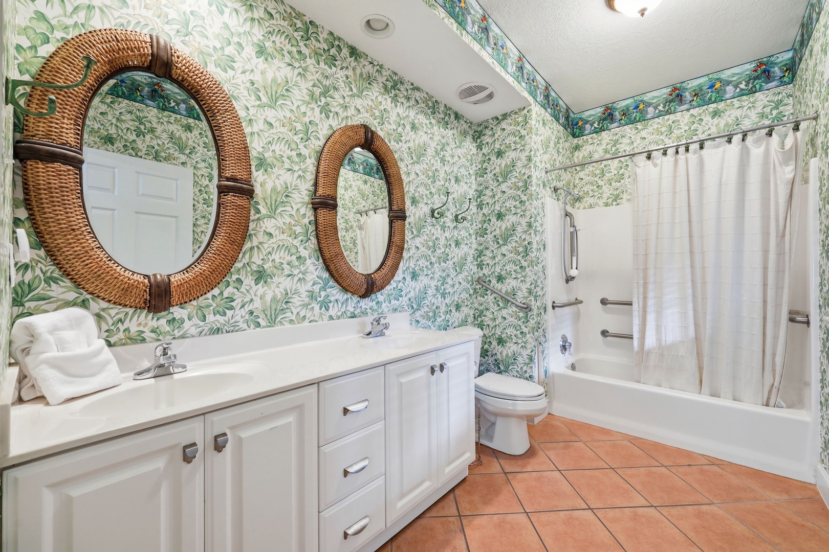 A bright bathroom featuring botanical wallpaper, dual wicker-framed mirrors, white vanity, and a tub-shower combo for your comfort.