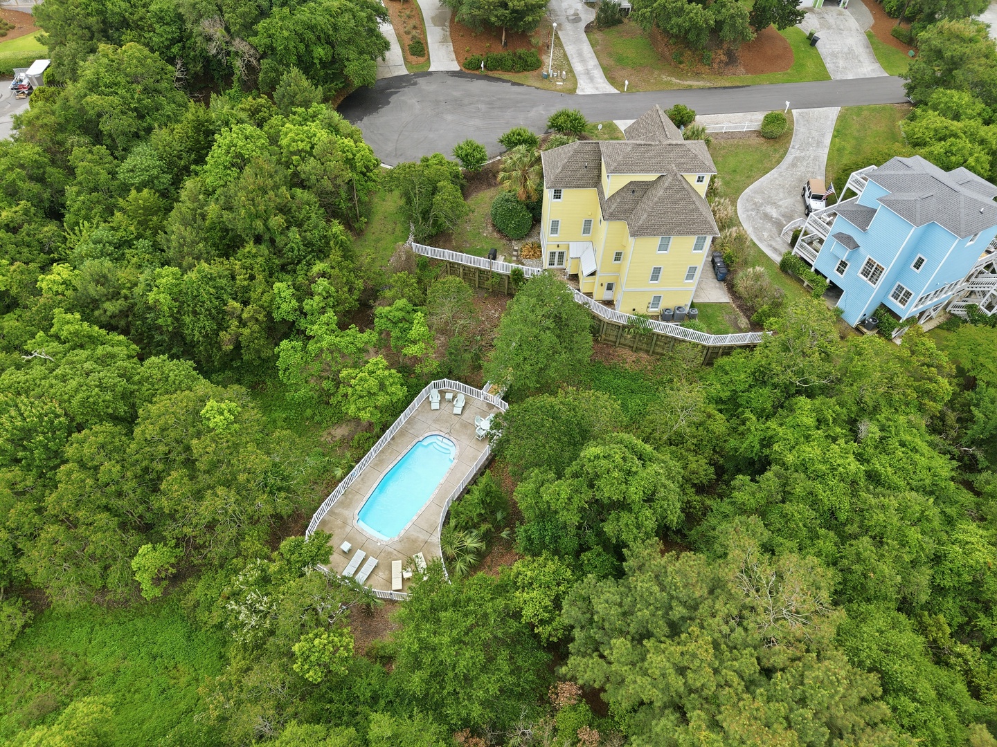 Aerial view showcasing the property and its inviting pool area, set within lush natural surroundings and a quiet residential neighborhood.