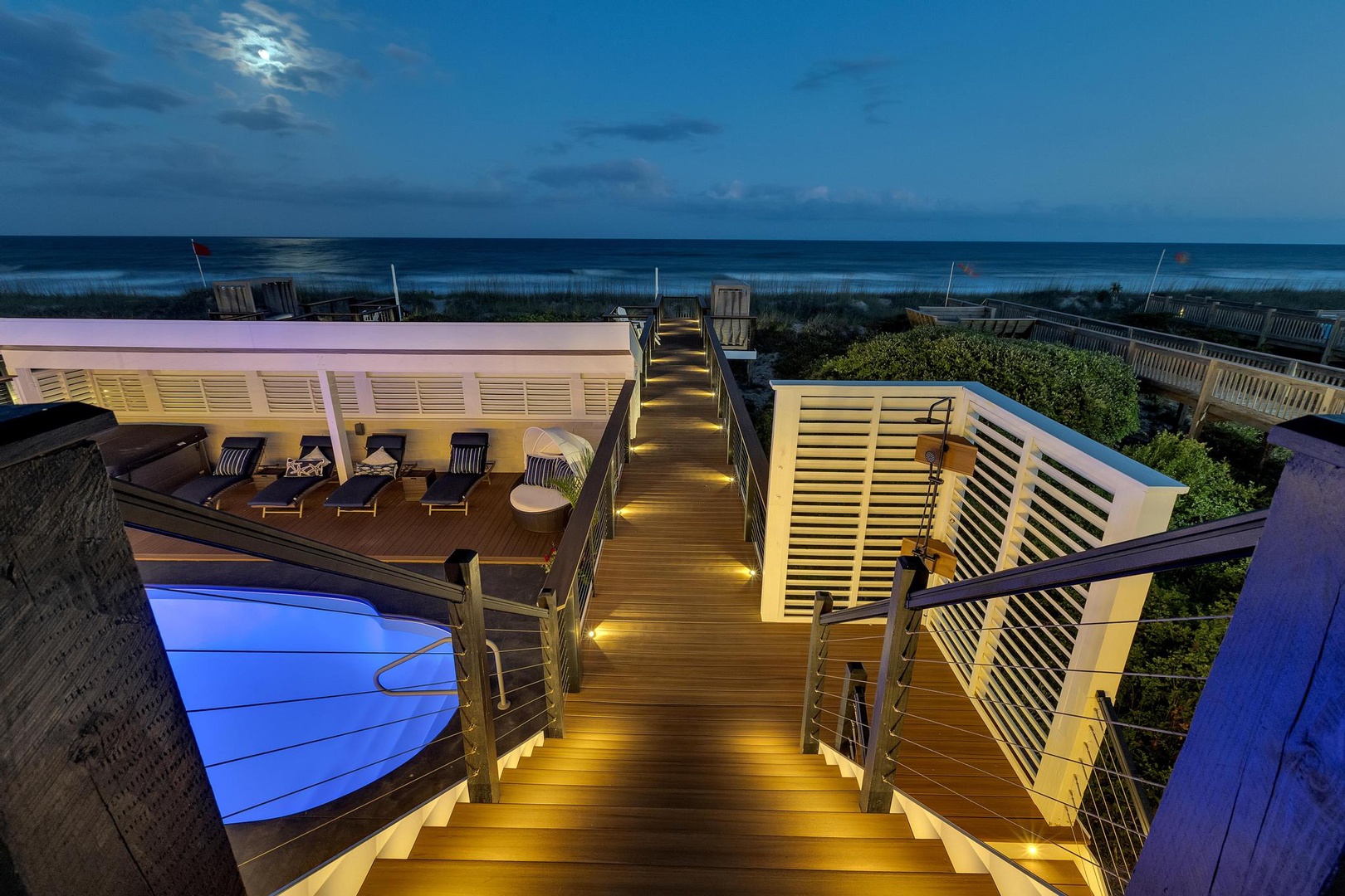 Spectacular rooftop deck showcasing breathtaking ocean views, illuminated steps, stylish lounge seating, and a glowing pool—perfect for unwinding under twilight skies.