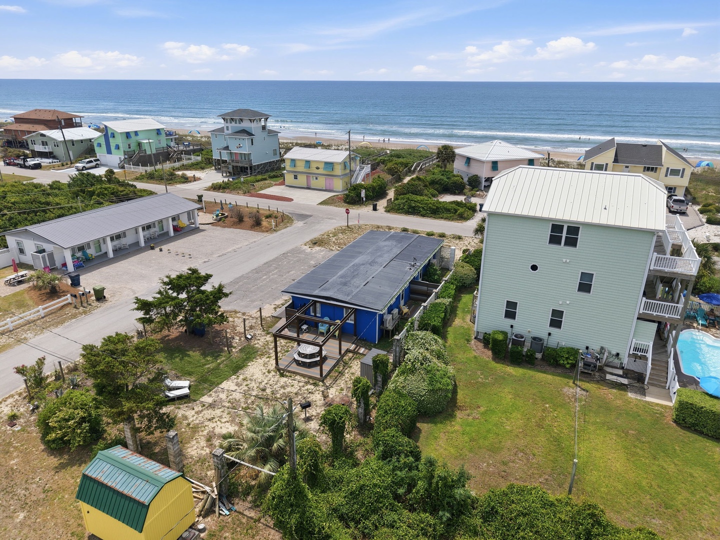 Aerial view of a beachside neighborhood featuring colorful coastal homes, a swimming pool, and direct beach access with the Atlantic Ocean visible in the background.