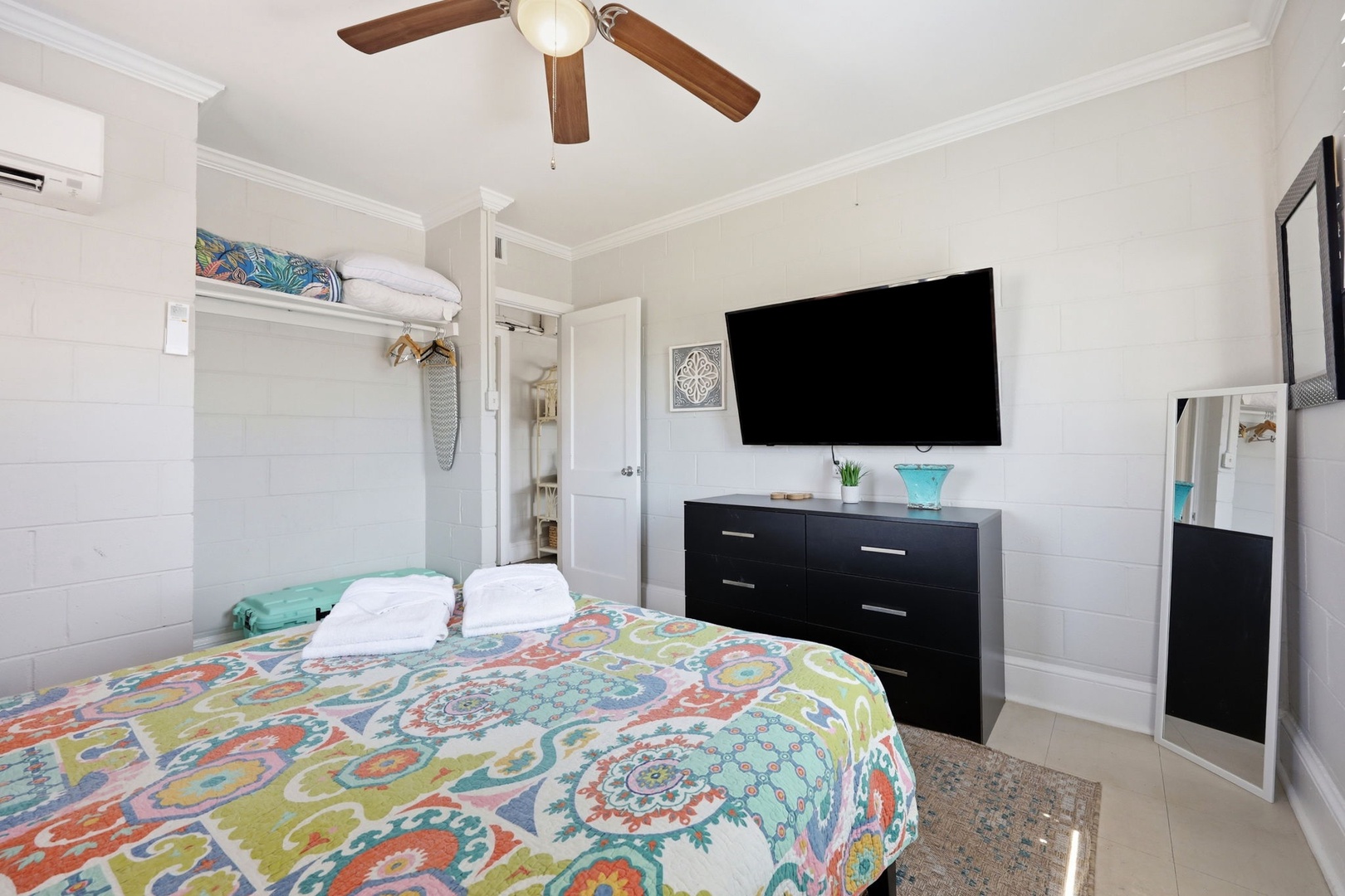 Relax in your bright, airy bedroom featuring a cozy bed with colorful linens, a wall-mounted TV for your entertainment, and a ceiling fan with climate control to keep you comfortable year-round.