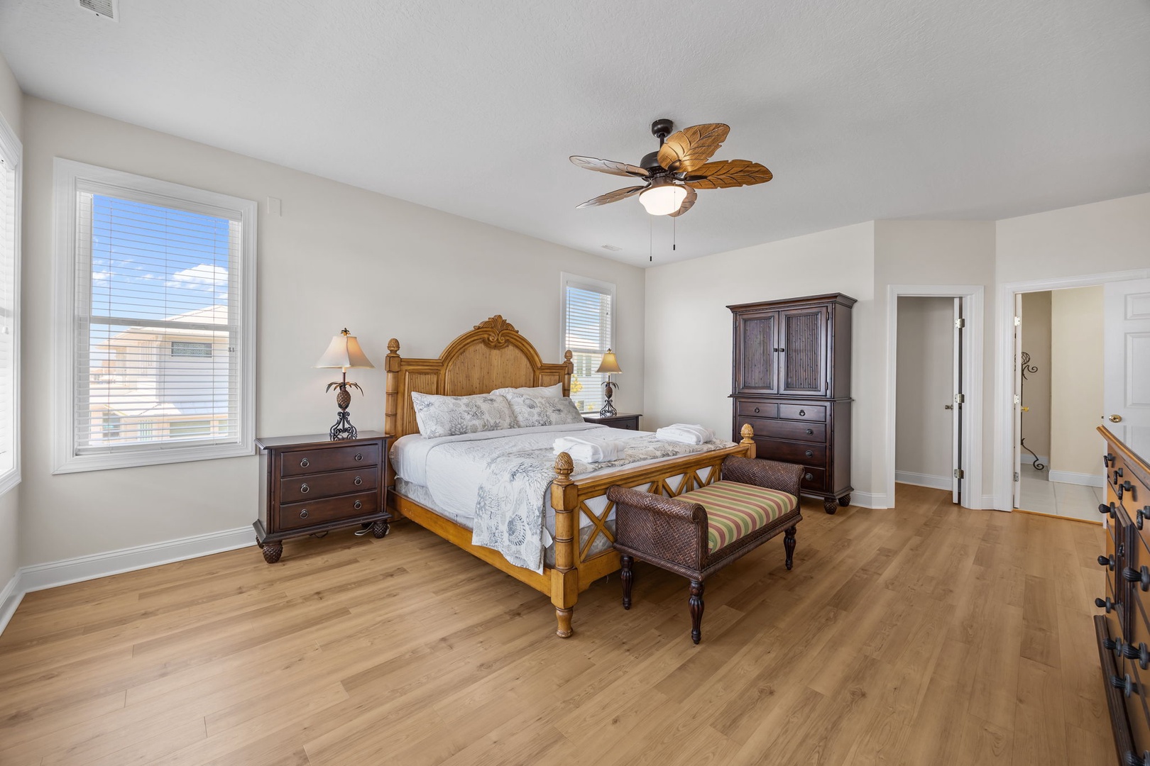 Relax in your spacious bedroom with warm wood floors, tropical ceiling fan, and elegant furnishings for a perfect coastal retreat.
