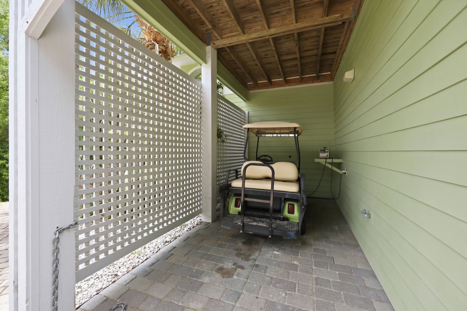 Covered parking area with latticed privacy screen and paver flooring—convenient golf cart storage adds easy mobility for local exploration.
