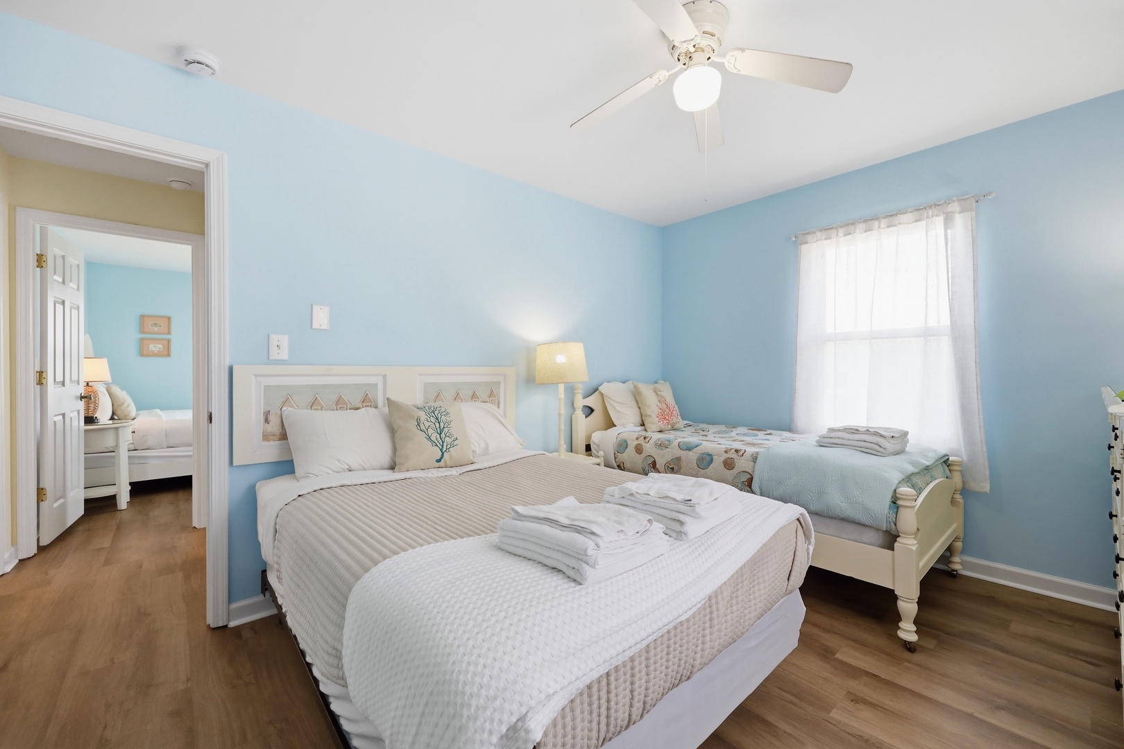 You'll love the calming coastal vibe of this airy bedroom, with soft blue walls, comfortable beds dressed in fresh linens, and a gentle breeze from the ceiling fan above.