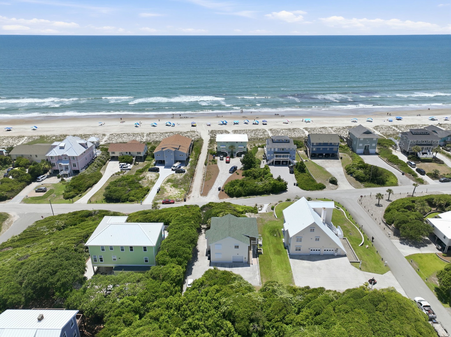 Aerial view showcasing beachfront vacation homes nestled along pristine sandy shores, with direct beach access and stunning ocean vistas stretching to the horizon.