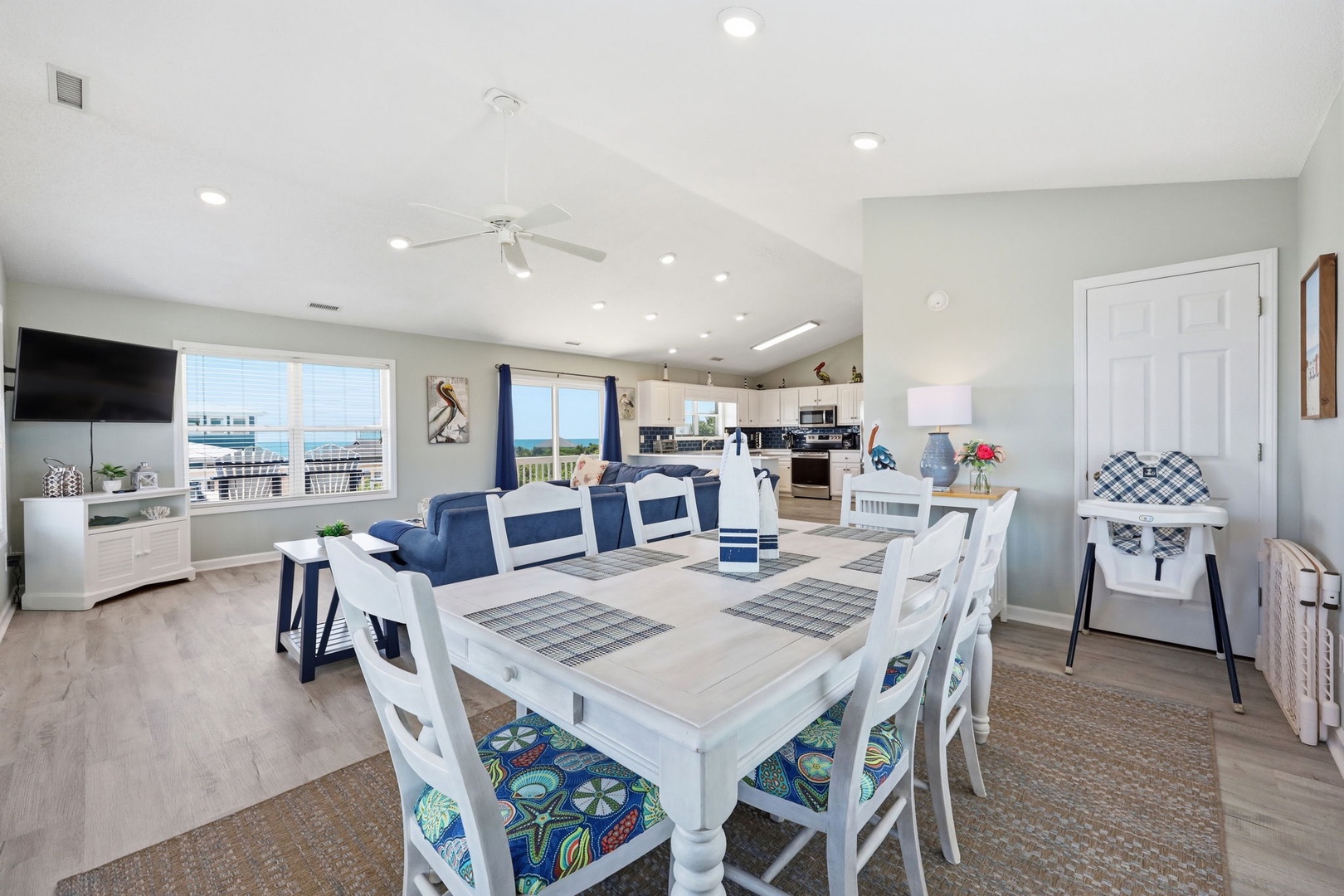 Gather around the spacious dining table with seating for eight, bathed in natural light from vaulted ceilings, as ocean breezes drift through this open-concept coastal retreat.