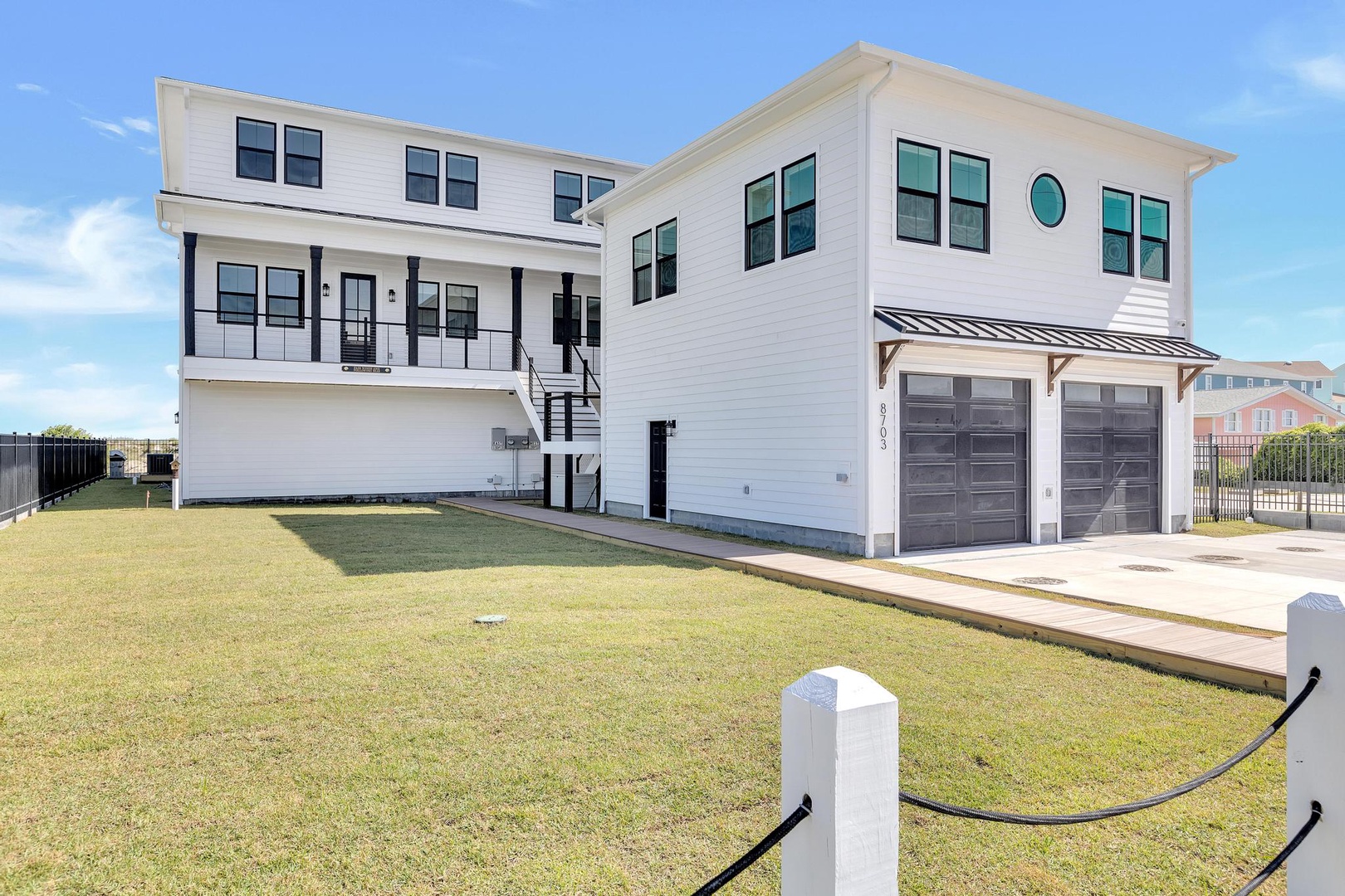 This modern coastal home features clean white siding, spacious covered decks, and a generous two-car garage, providing a bright and welcoming arrival experience for guests.