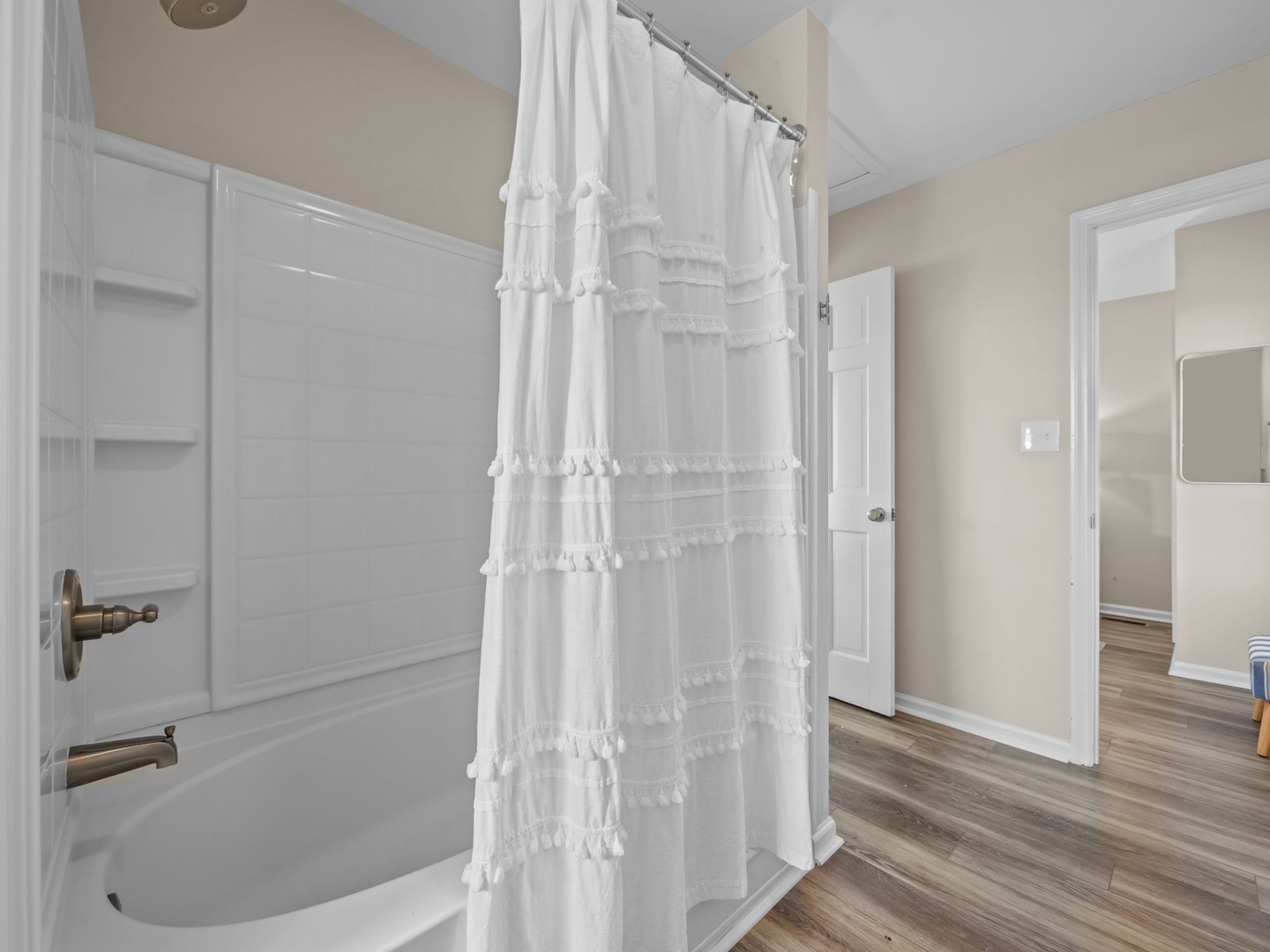 Step into your bright, clean bathroom featuring a spacious tub-shower combo with charming ruffled curtain and beautiful flooring throughout.