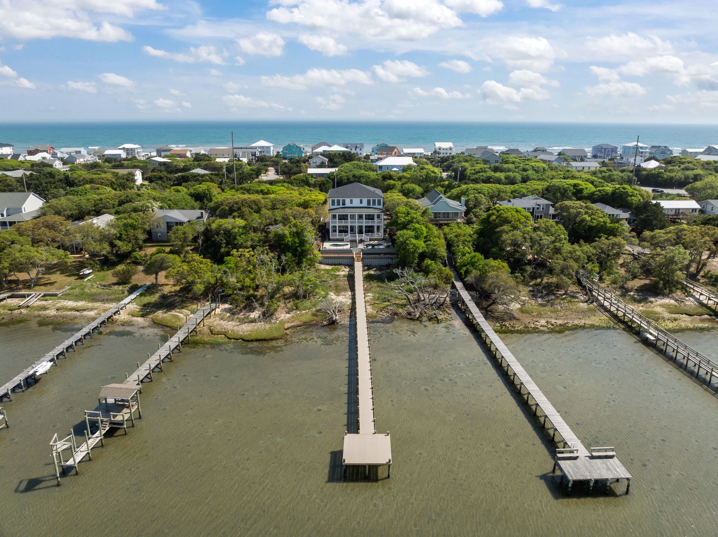 Elevated coastal property with private dock extending into calm waters, surrounded by mature trees and beachfront community.