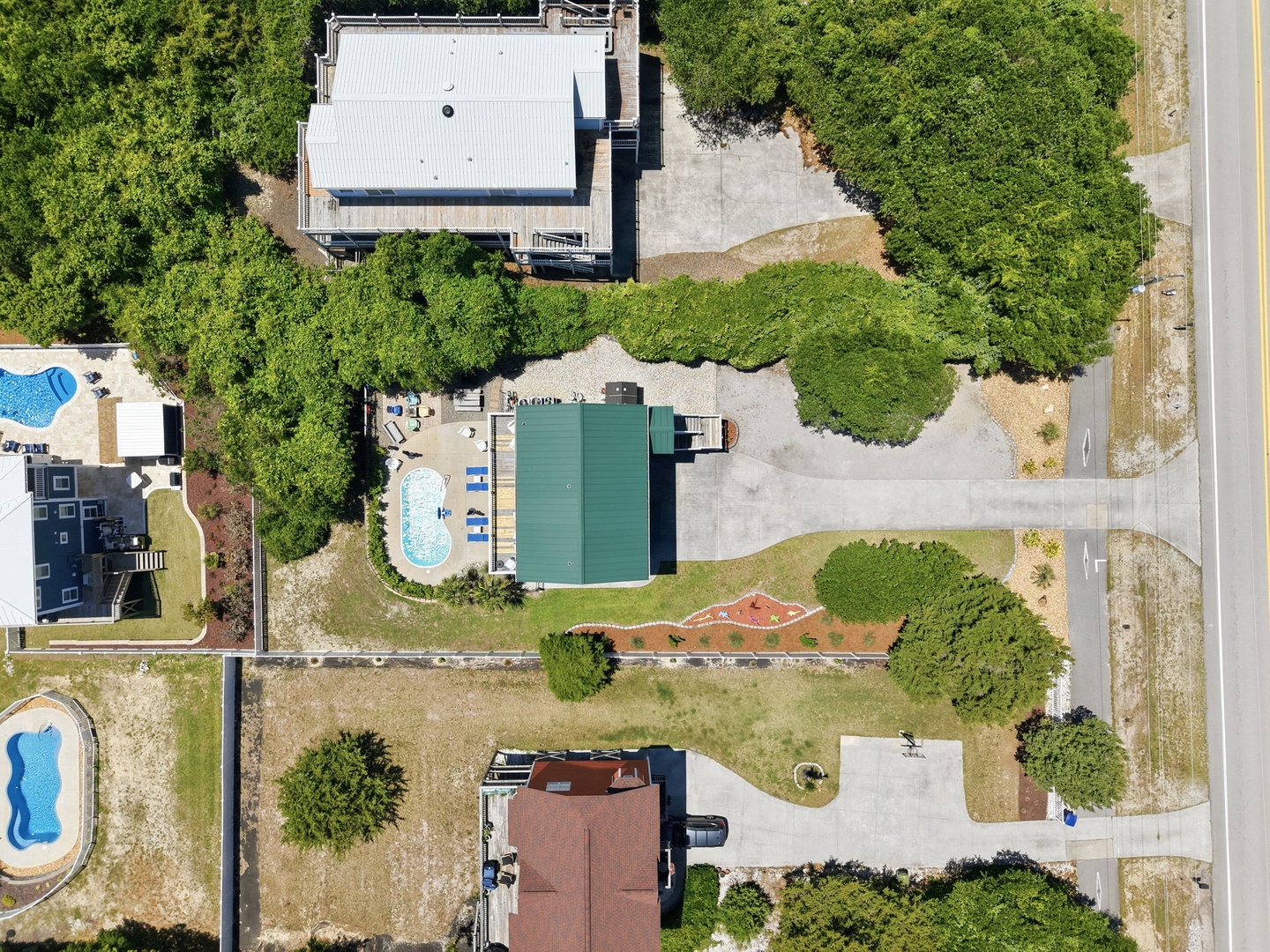 Aerial view of a vacation rental property surrounded by lush greenery, featuring a swimming pool and spacious grounds, located in a quiet residential neighborhood.