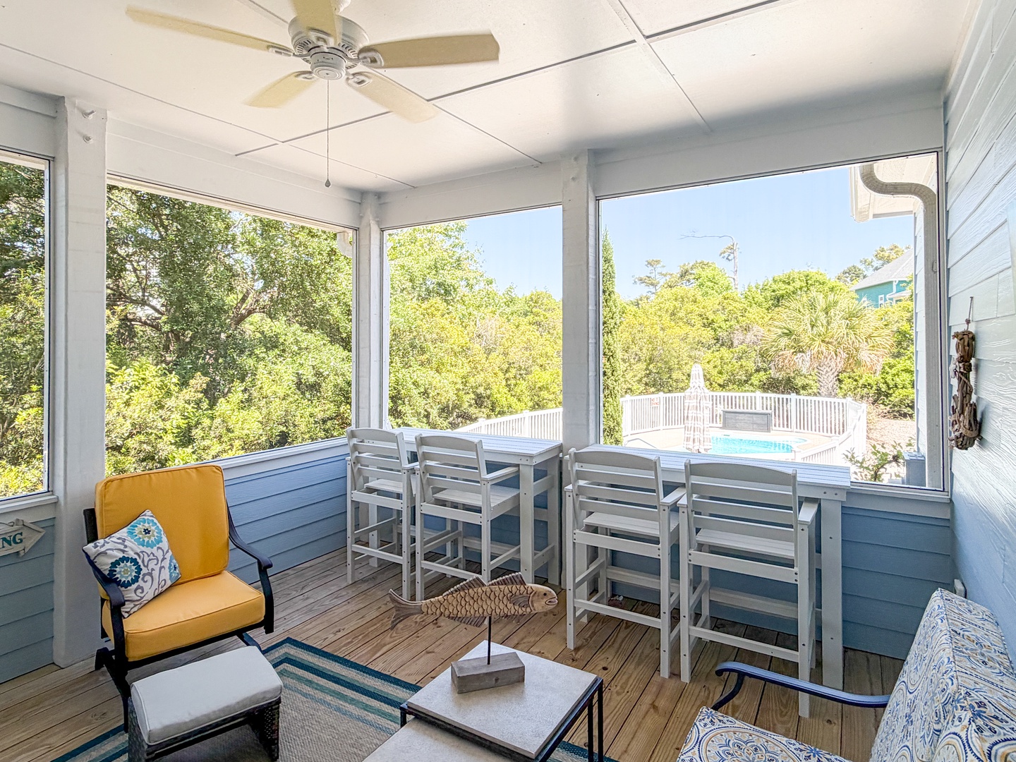 Picture yourself gathered around the dining table with loved ones, the ceiling fan gently circulating the breeze as sunlight streams through expansive windows framing lush trees and your private pool just beyond the glass.