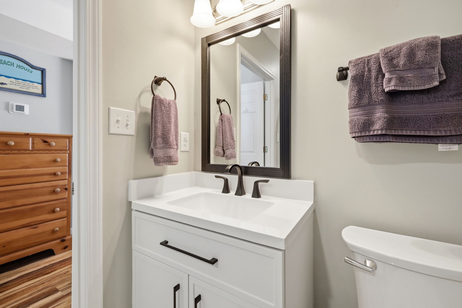 Freshen up in this bright, welcoming bathroom with soft purple towels, modern fixtures, and a clean vanity—your perfect retreat after a beach day.