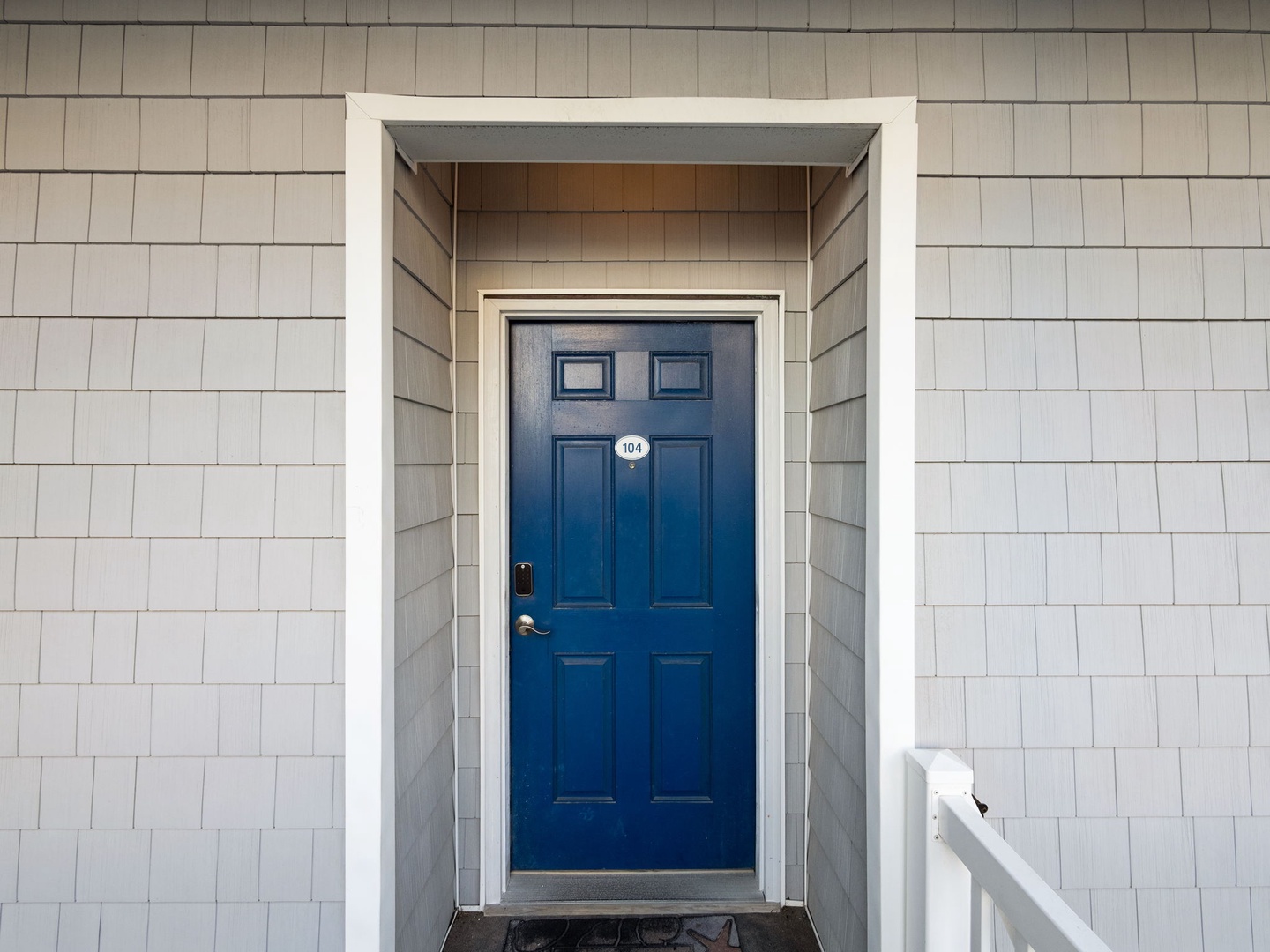 Classic coastal-style entrance featuring a striking blue door and weathered shingle siding that welcomes guests to unit 404.
