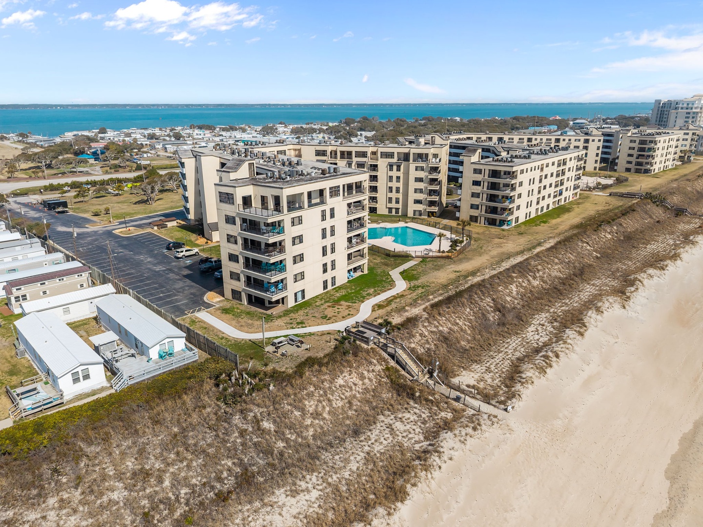 Beachfront property situated directly on sandy shores with pool access, neighboring residential areas, and scenic coastal water views.