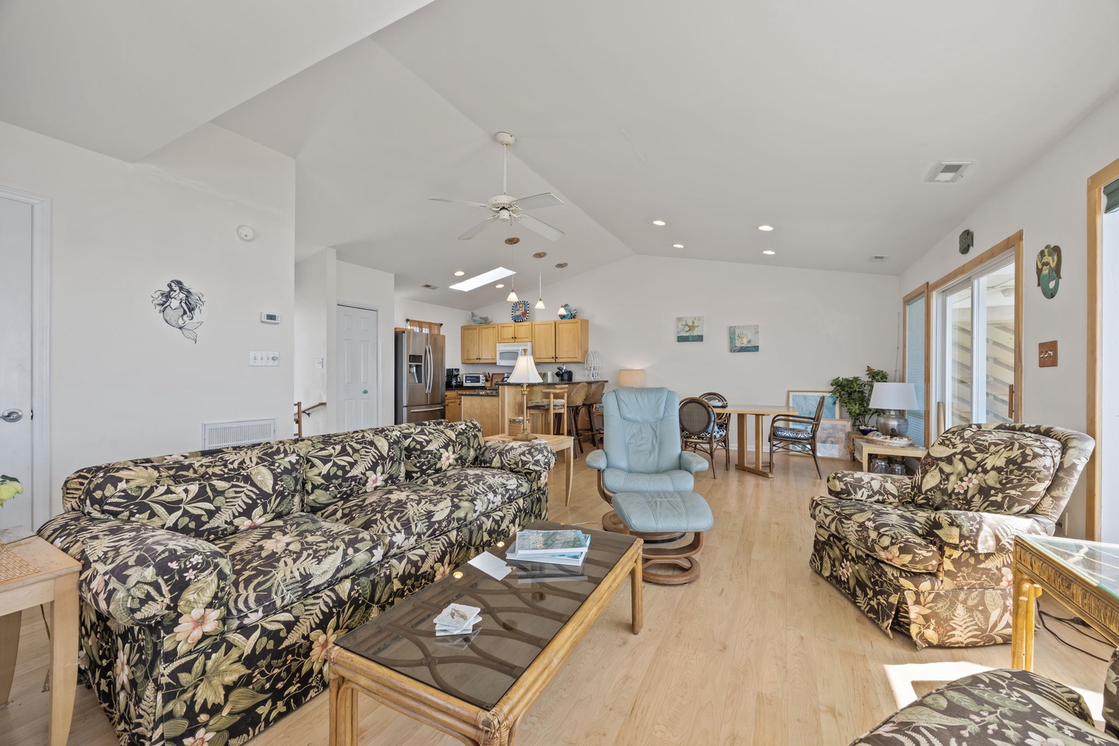 Relax in your spacious open-concept living area with tropical-print seating, modern kitchen, and bright dining space perfect for gathering.