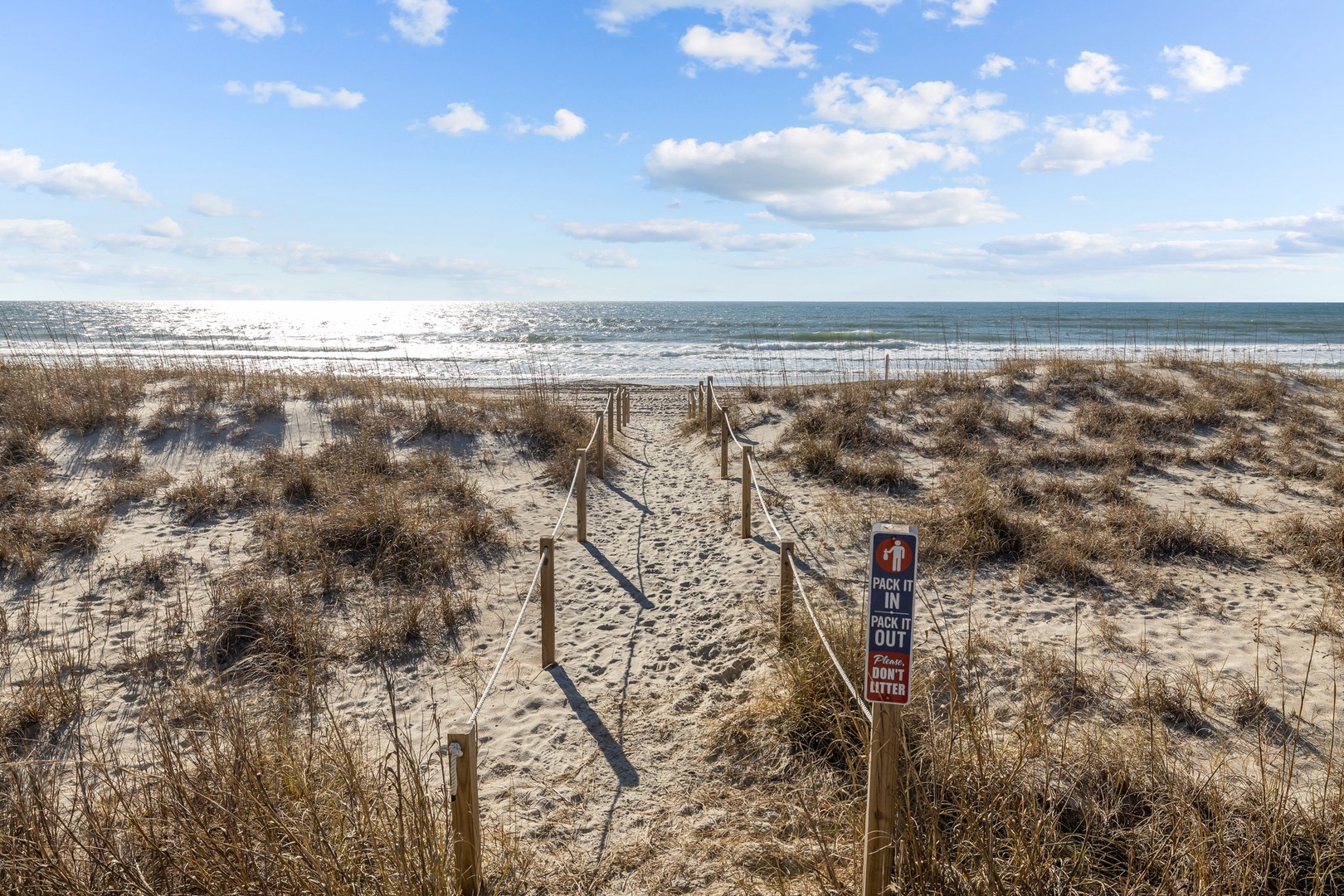 A pristine beach access trail leads through protected dunes to sparkling ocean waves under blue skies.