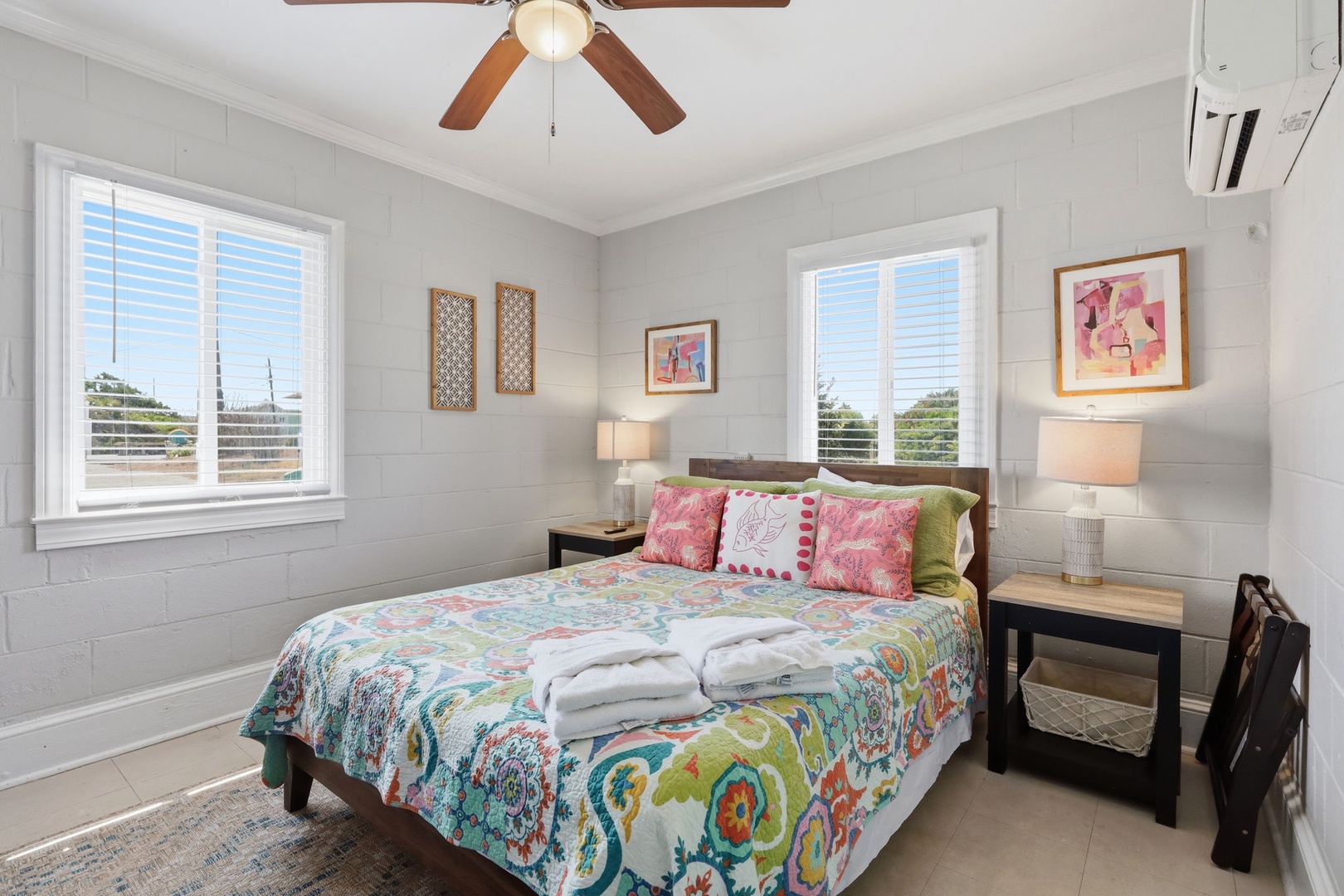 Step into your bright, airy bedroom where white shiplap walls and cheerful linens create a coastal sanctuary. Fresh towels await your arrival, while the ceiling fan and AC keep you cool as you unwind.