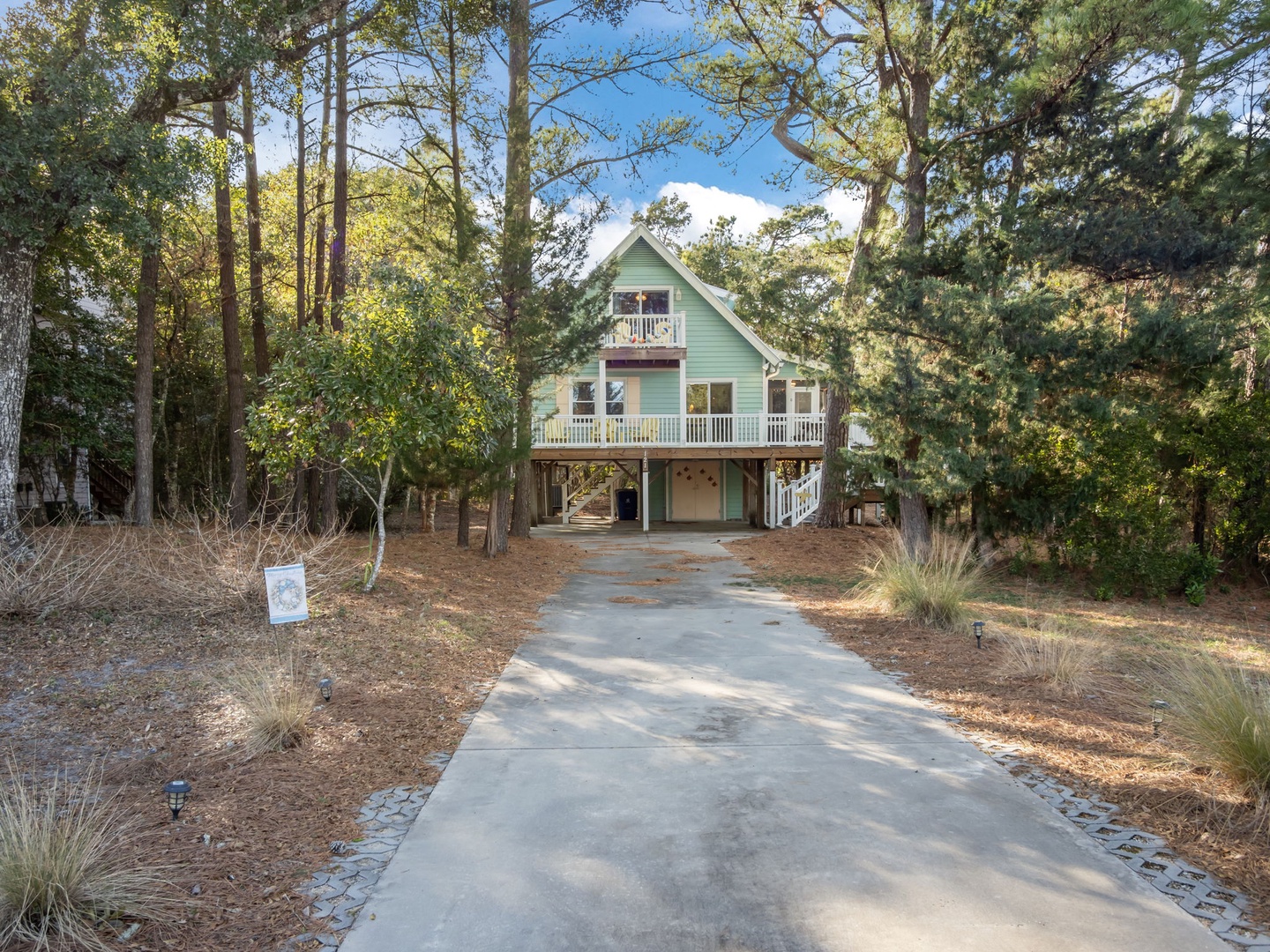 A charming coastal cottage nestled among tall pines, featuring multiple decks and a welcoming driveway leading to your peaceful forest retreat.