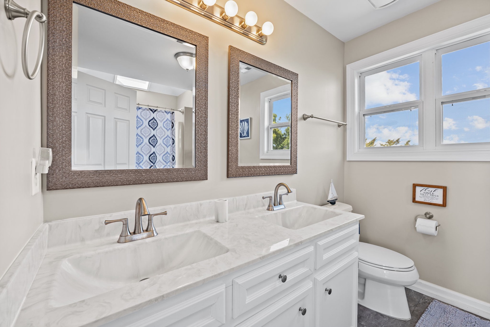 Refresh in this elegant dual-sink bathroom with marble countertops, stylish mirrors, and bright natural light streaming through the windows.