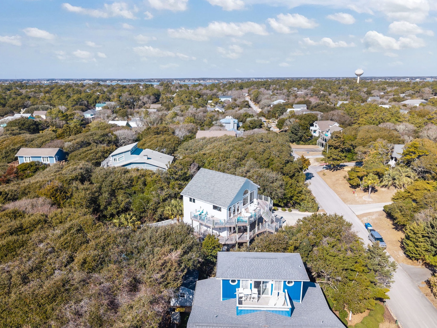 Aerial view of coastal vacation homes nestled among lush trees in a peaceful residential neighborhood near the shore.