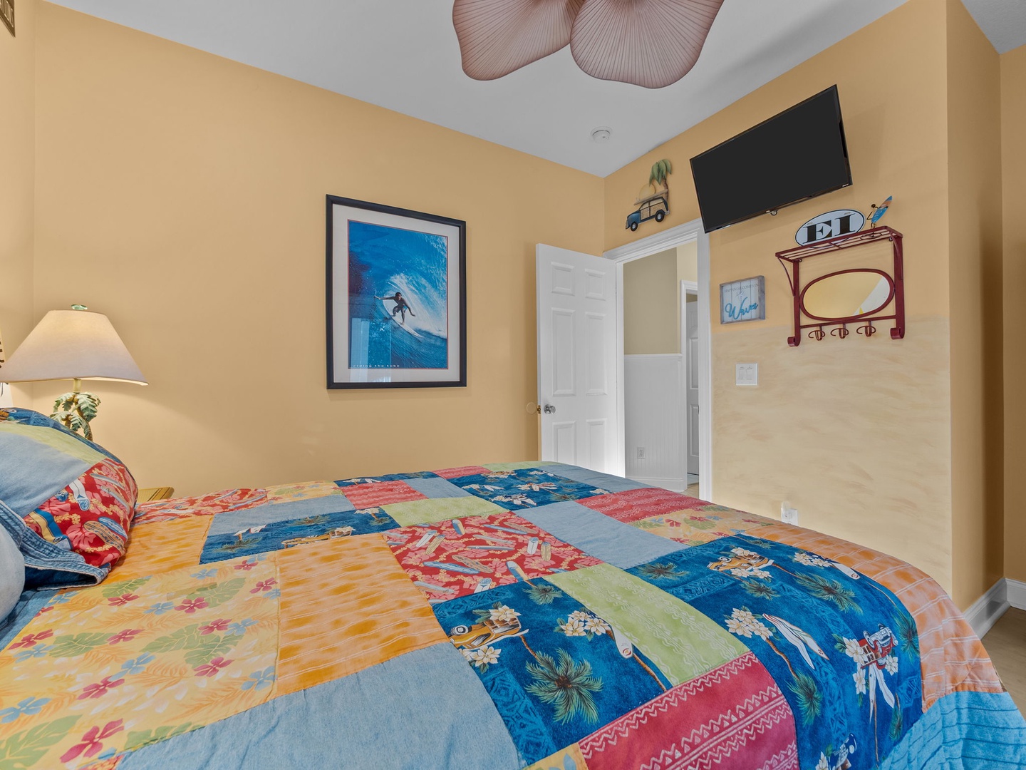 Relax in your colorful bedroom with tropical-themed bedding, wall-mounted TV, and charming surf artwork creating a cheerful coastal atmosphere.