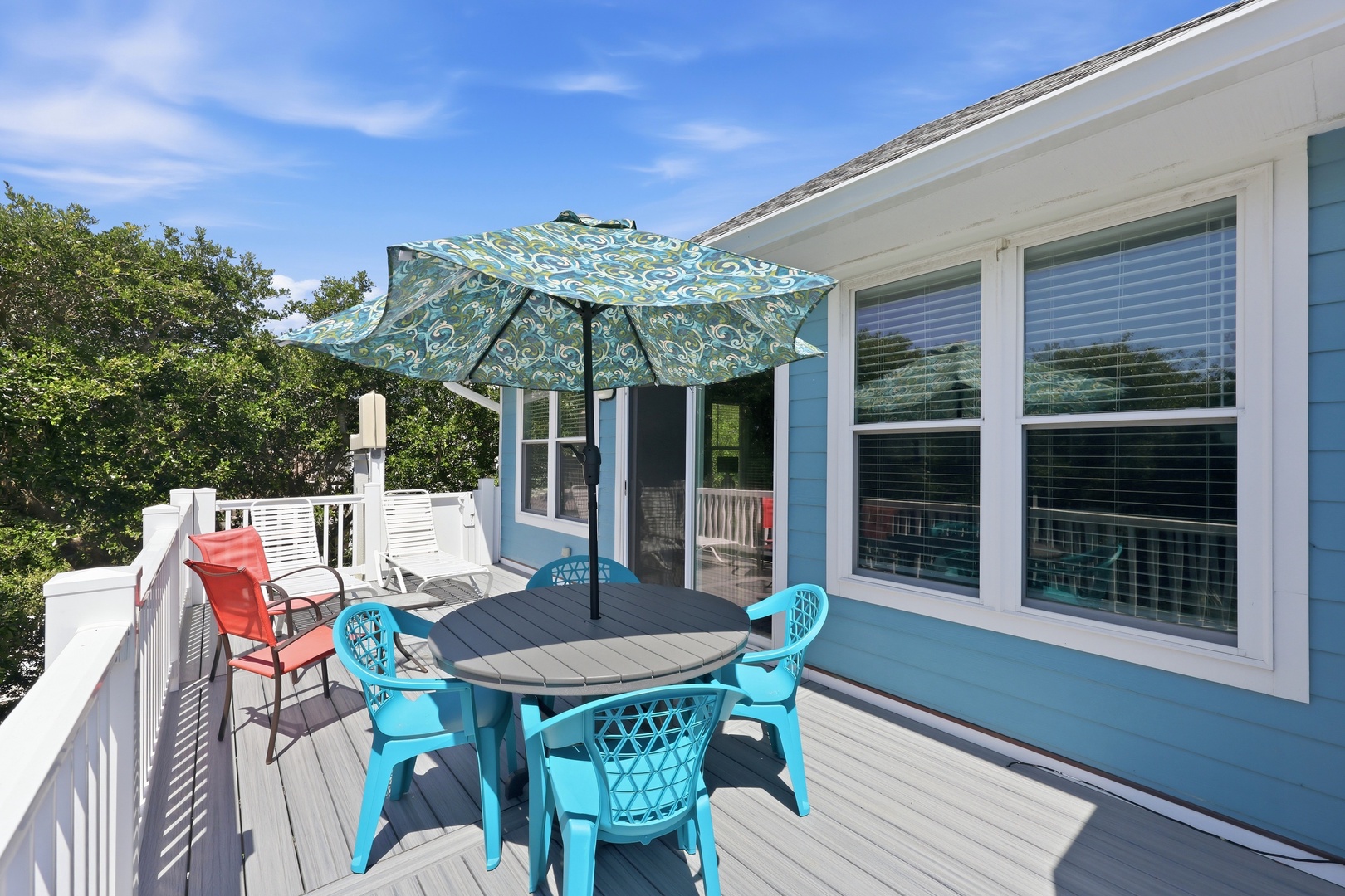 Enjoy morning coffee or evening meals on your private deck, complete with comfortable seating, cheerful turquoise dining set, and a shaded umbrella perfect for sunny afternoons overlooking lush greenery.