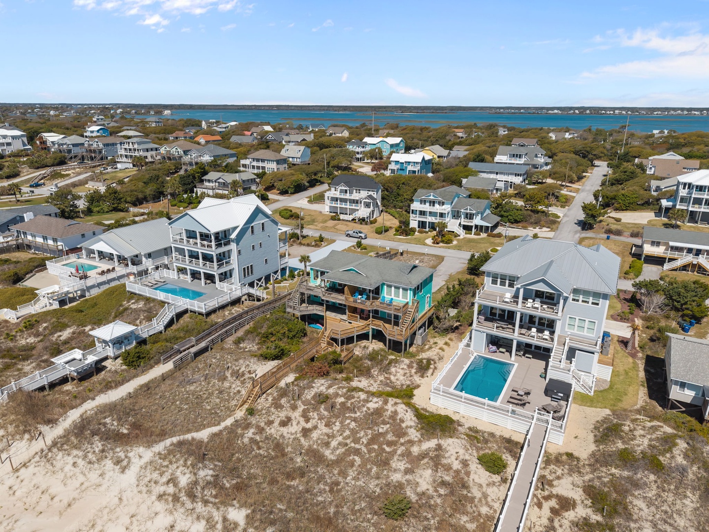Aerial view of coastal vacation homes with swimming pools nestled among beach community neighborhoods near the sparkling waterfront.