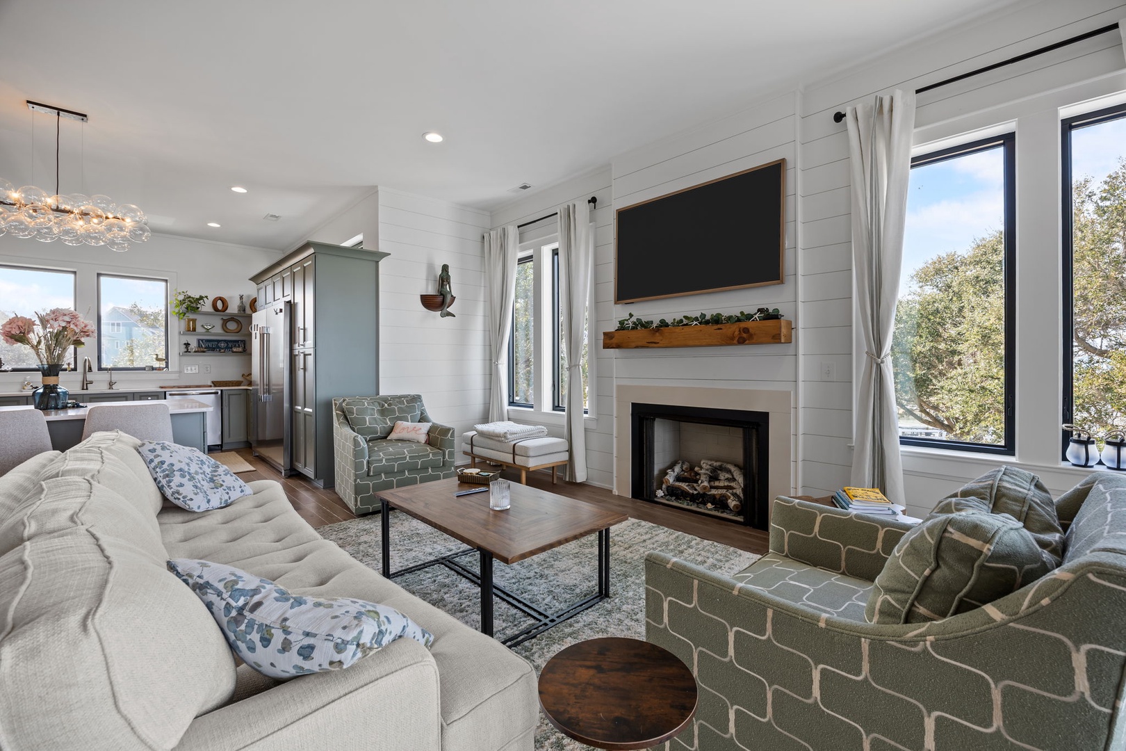 Gather by the fireplace in this bright living room, where modern comfort meets rustic charm with shiplap walls and treetop views.