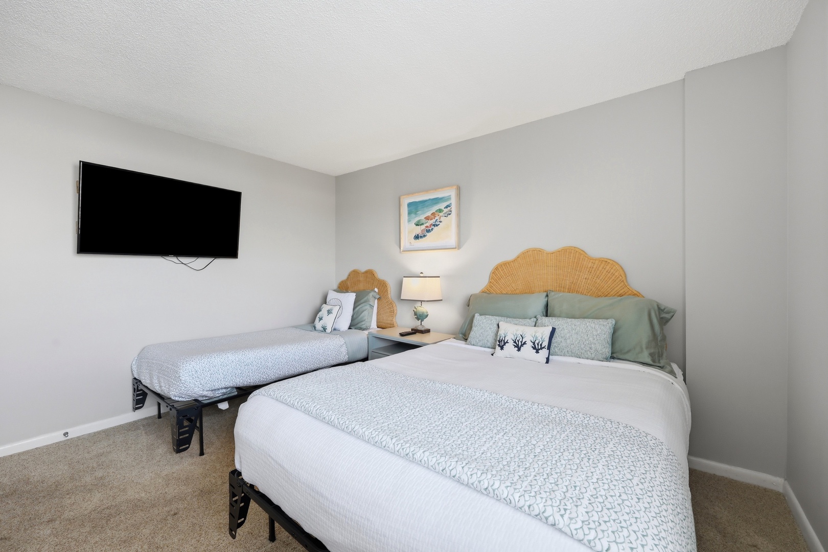 Your coastal-inspired retreat features two plush beds with woven rattan headboards, serene ocean-toned linens, and a wall-mounted TV for your entertainment. Drift off to the gentle seaside palette surrounding you.