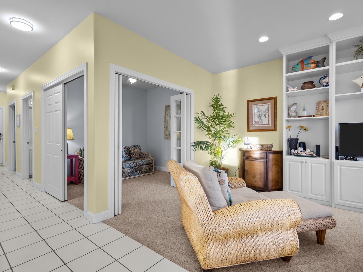 Unwind in your spacious living area with wicker armchairs, entertainment center, and tranquil decor creating the perfect coastal retreat atmosphere.