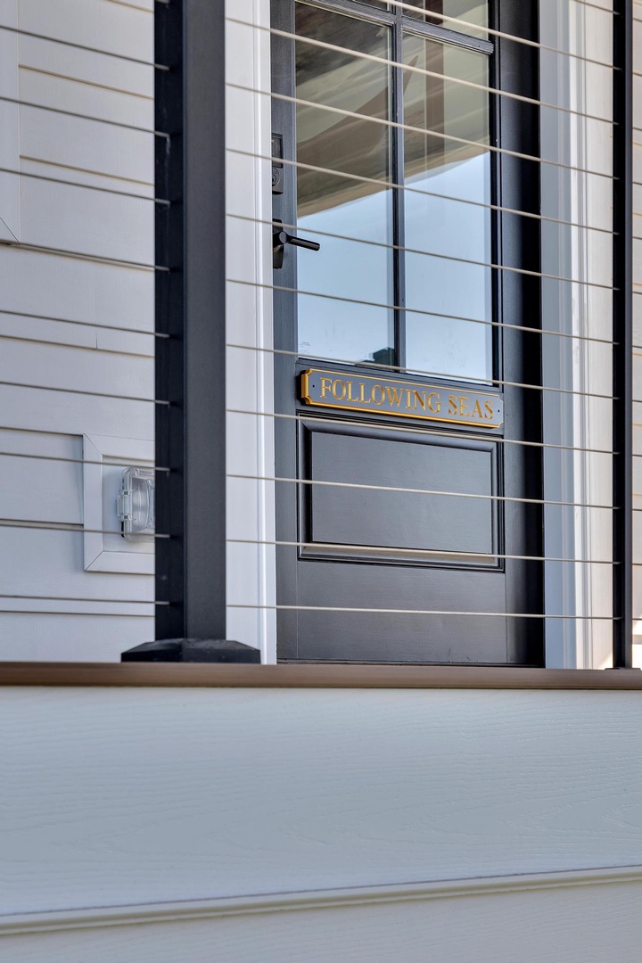 The entrance features a modern design with black-framed glass doors and elegant brass signage marking your arrival at Following Seas.