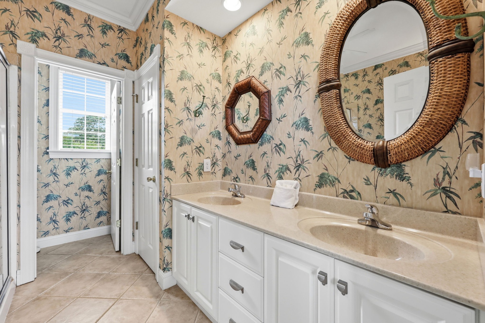 Refresh in your elegant dual-sink bathroom with charming tropical wallpaper, abundant natural light, and thoughtful coastal touches that bring relaxed island vibes to your daily routine.