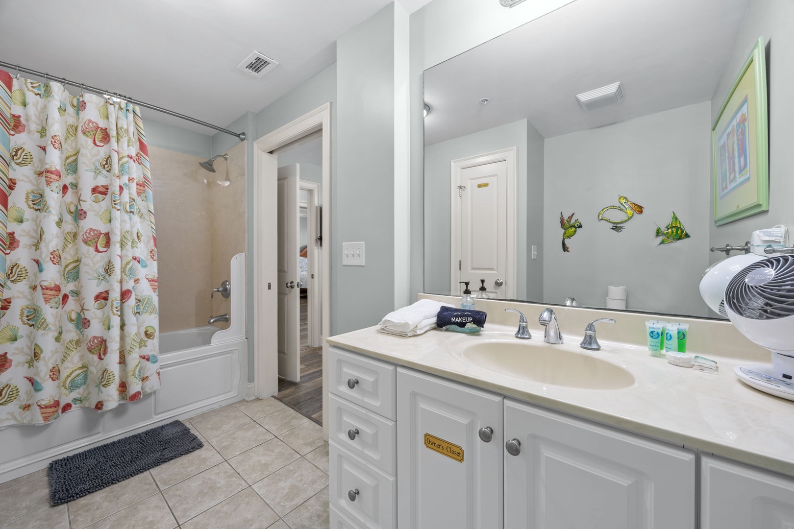 Your spacious bathroom features a relaxing tub with tropical fish shower curtain, well-lit vanity with fresh amenities, and thoughtful nautical touches throughout.