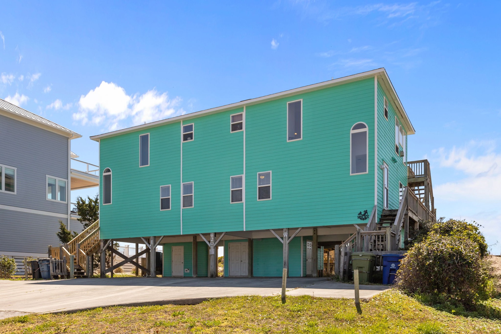 Coastal rental home featuring bright turquoise siding and elevated design, situated in a charming beachside neighborhood.