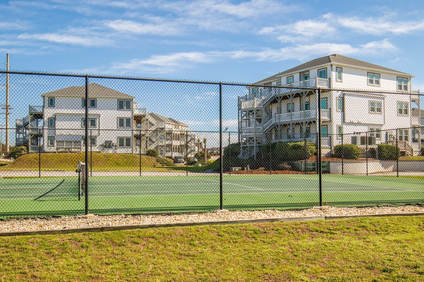 Tennis court with surrounding residential buildings in a coastal neighborhood setting.