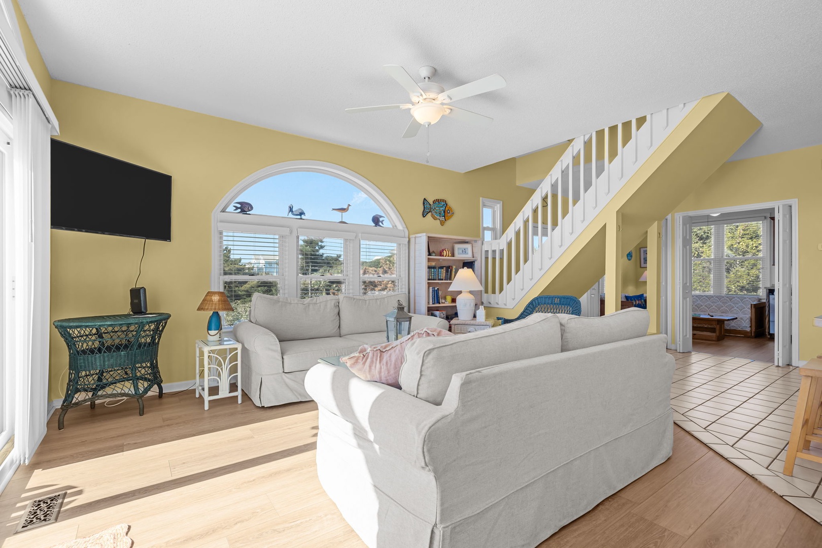Relax in this bright coastal living room with comfy sofas, ceiling fan, and charming arched window that frames peaceful views.