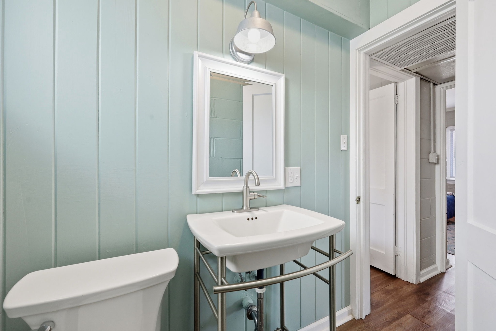 Step into your serene coastal-inspired bathroom with soft seafoam paneling, a classic pedestal sink, and warm hardwood floors that welcome you home after a day of exploring.