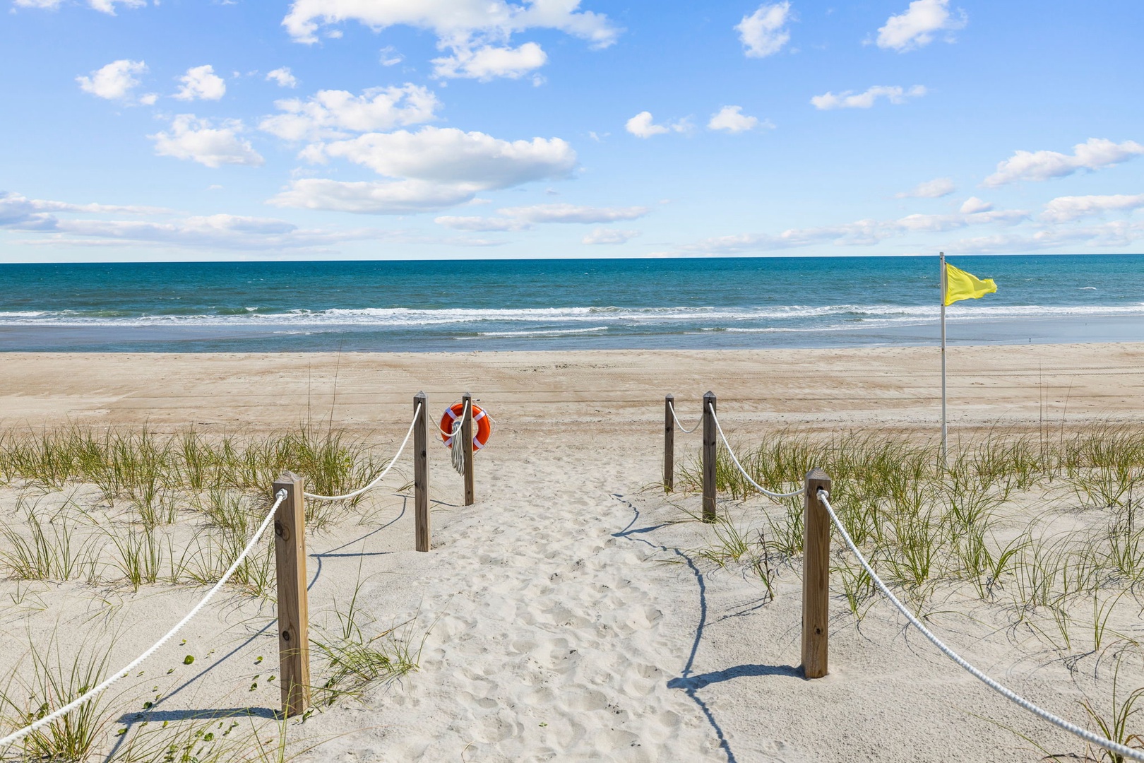 Pristine beach with protected dunes featuring wooden boardwalk access and safety flag for swimming conditions.