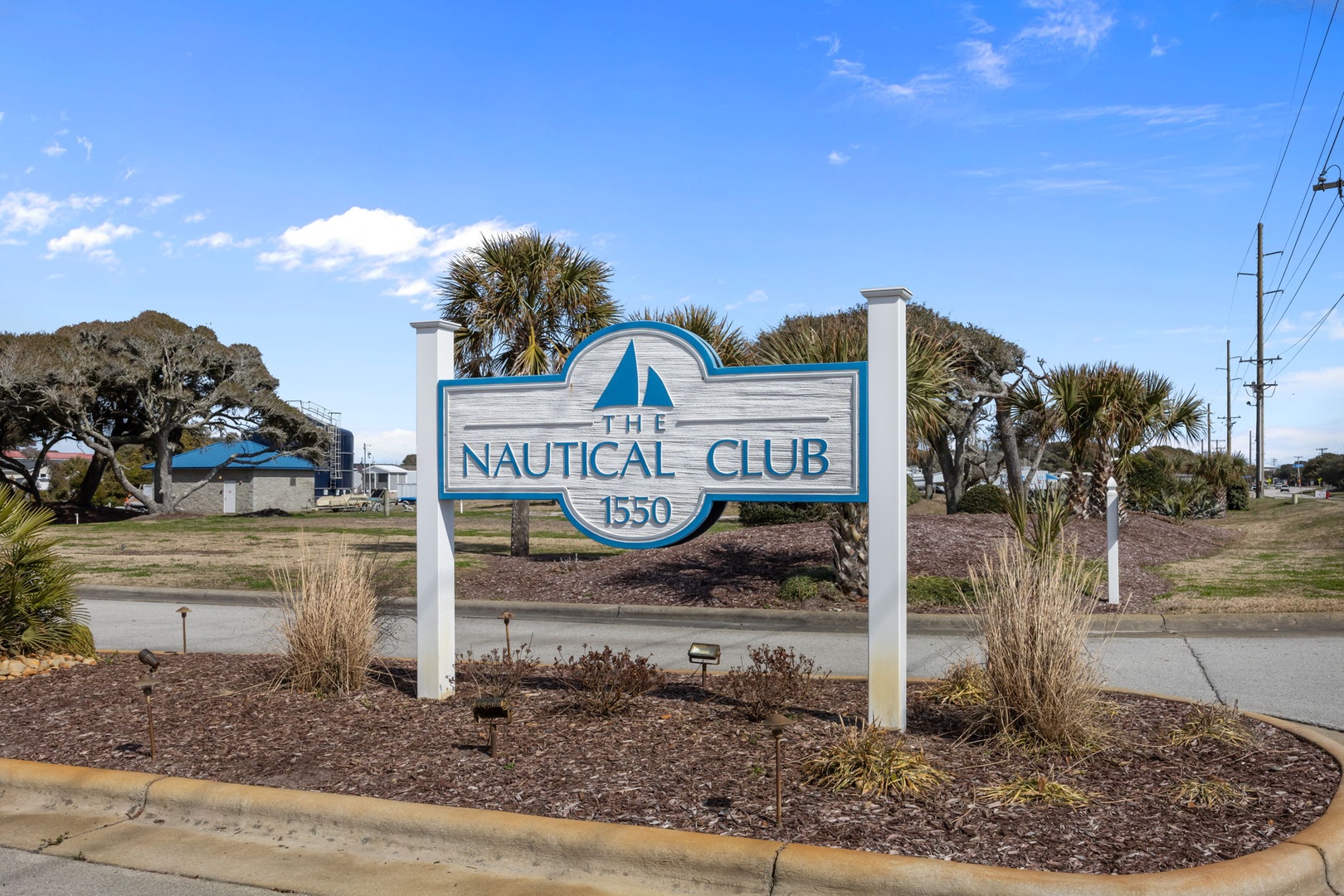 The Nautical Club property entrance sign welcomes guests to this coastal retreat surrounded by palm trees and natural landscaping.