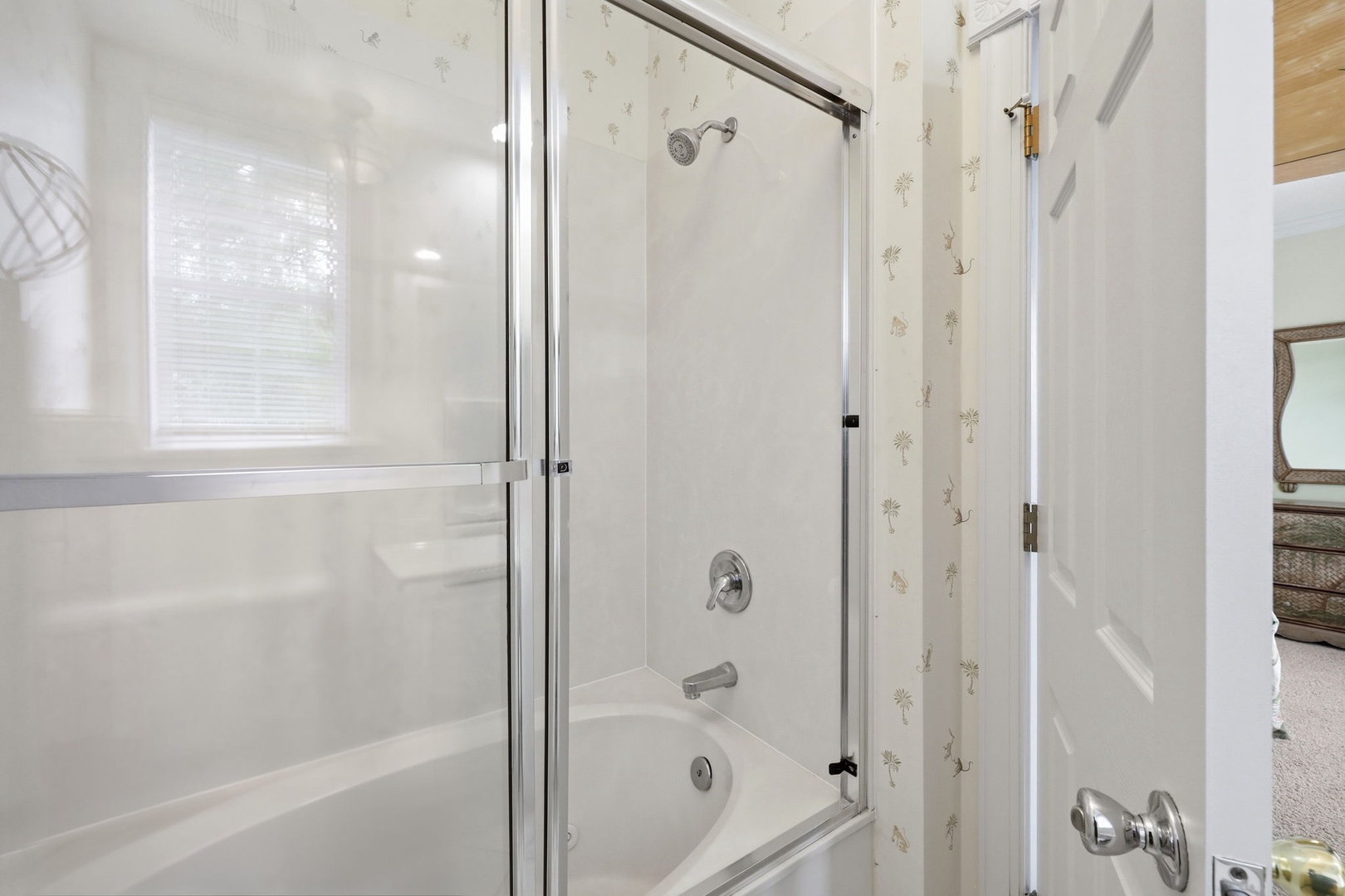 A bright, spotless bathroom with a tub-shower combo awaits your morning routine—glass doors, clean tiles, and natural light for a refreshing start.