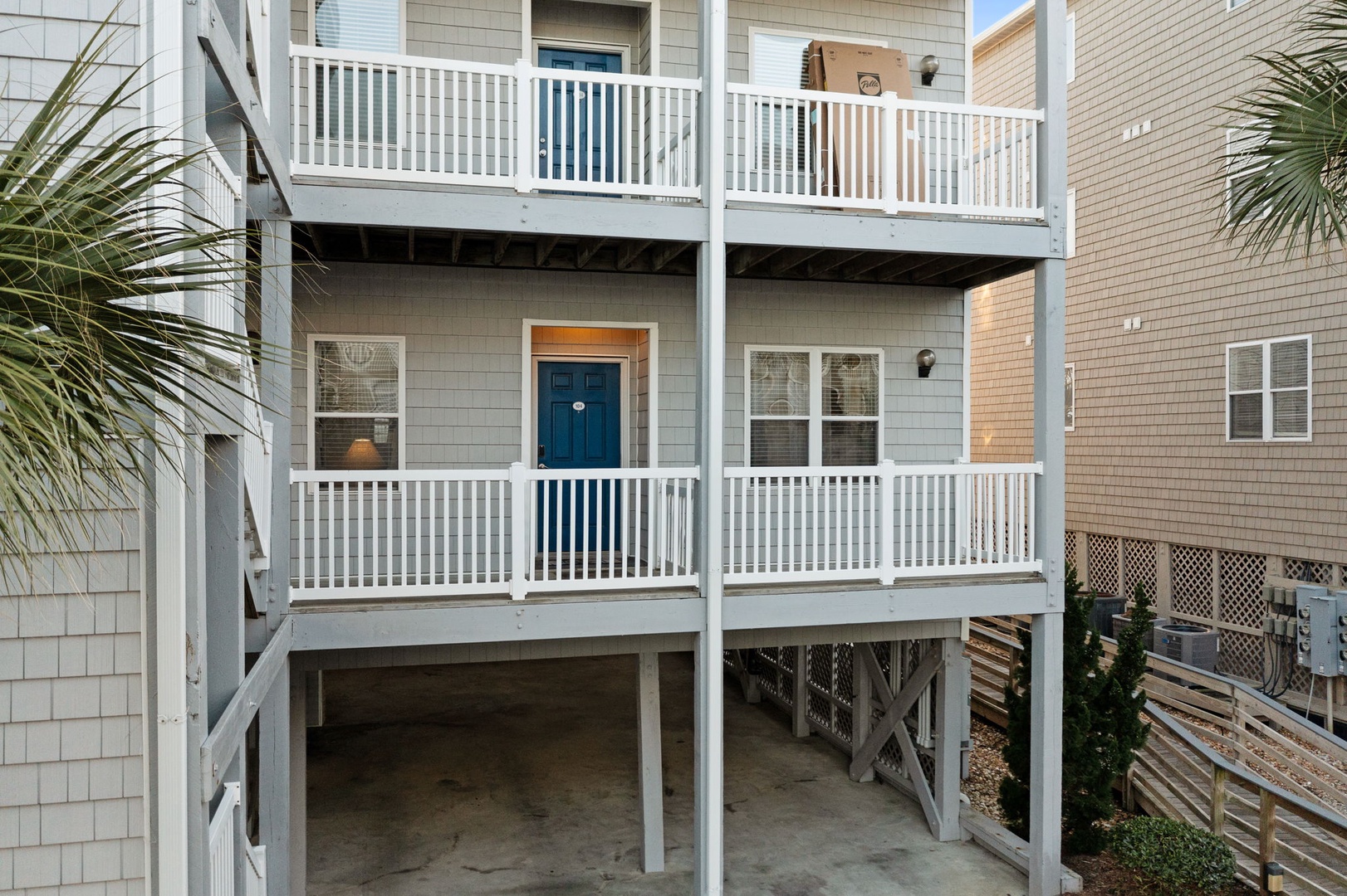 Multi-level beach house featuring white railings, blue door, and covered parking below.