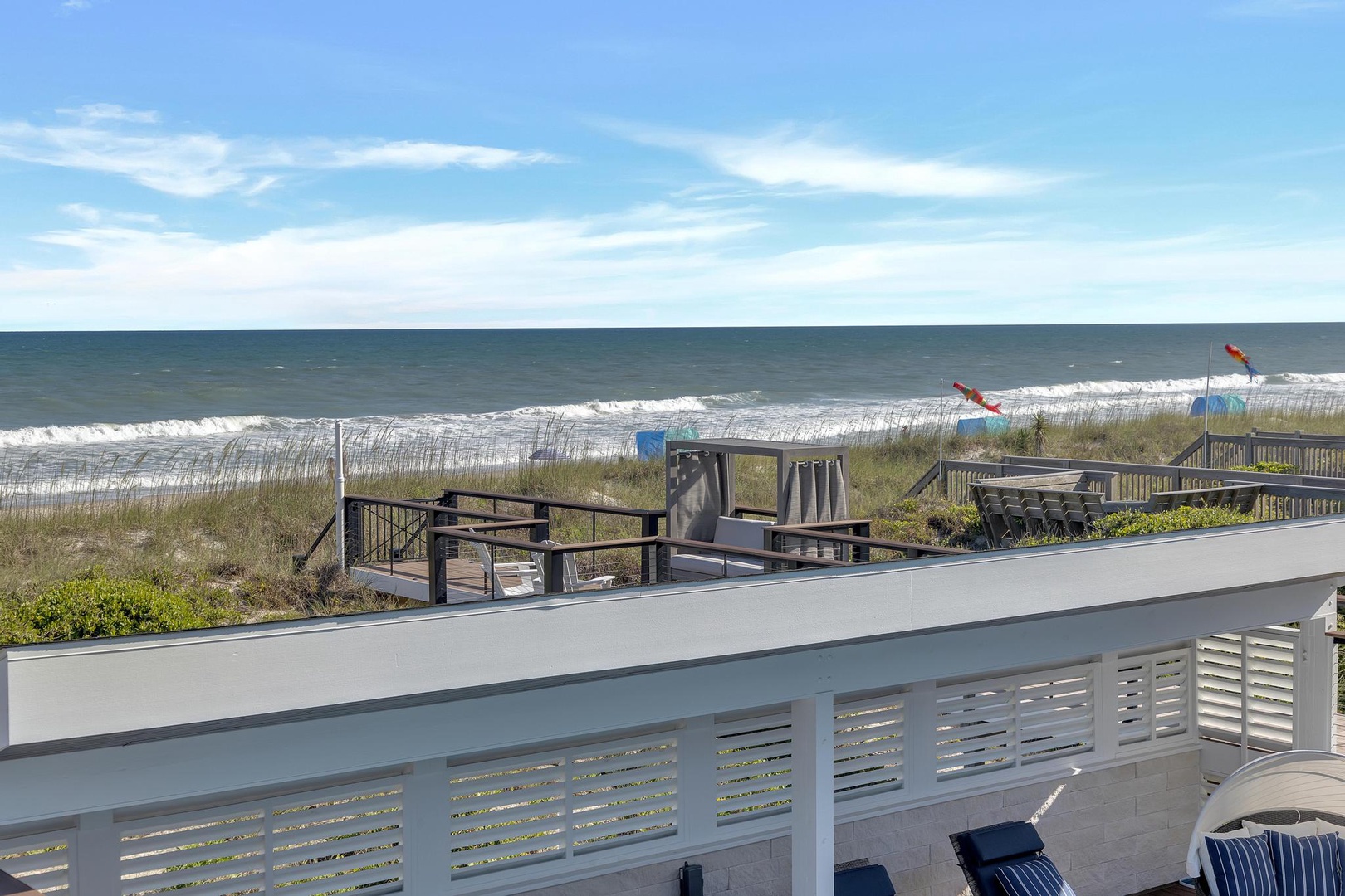 Oceanfront location with direct beach access and coastal views, featuring pathways through dunes and gentle waves rolling onto sandy shores under clear blue skies.