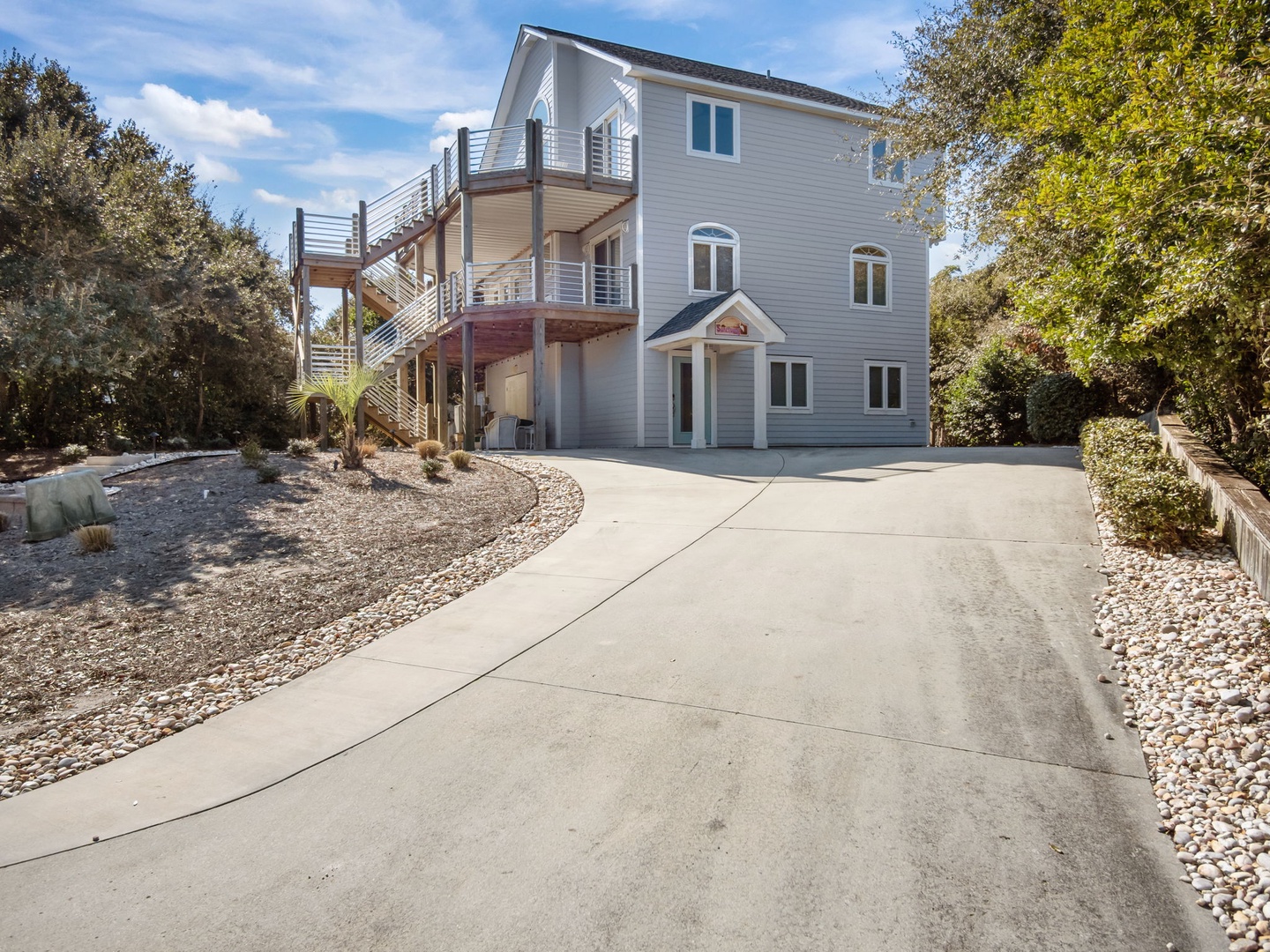 Spacious three-story coastal home with exterior stairs and private parking nestled among mature trees.