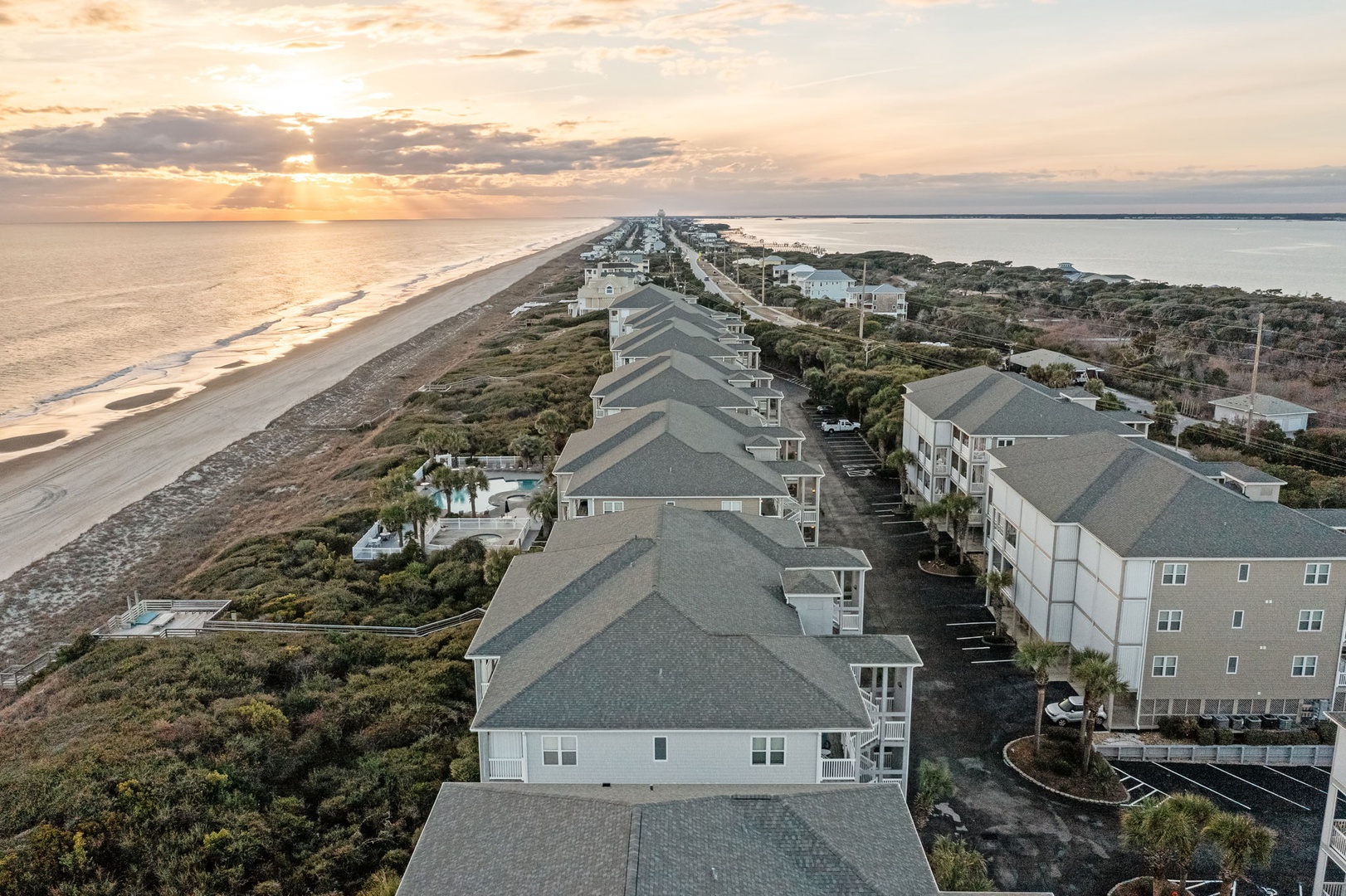 Aerial view of beachfront vacation rentals nestled along pristine coastline at sunset, offering direct beach access and ocean views.